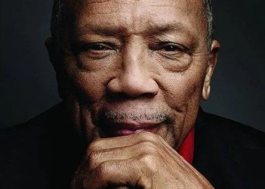 Close-up portrait of composer and producer Quincy Jones resting his chin on his hand.