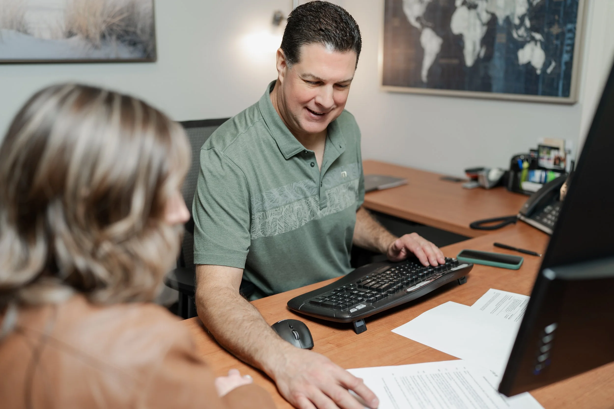 Man and woman in an office discussion, with documents and computer on desk.