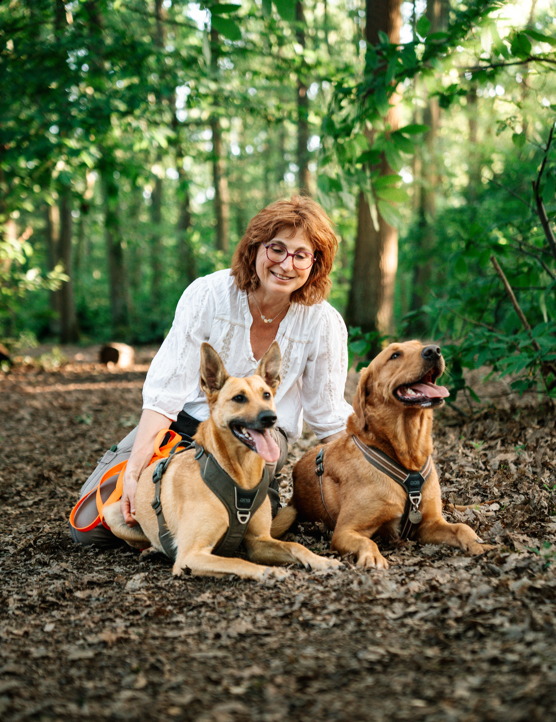 Sandrine, fondatrice de MuZo Futé, avec deux chiens en forêt dans une approche respectueuse du chien