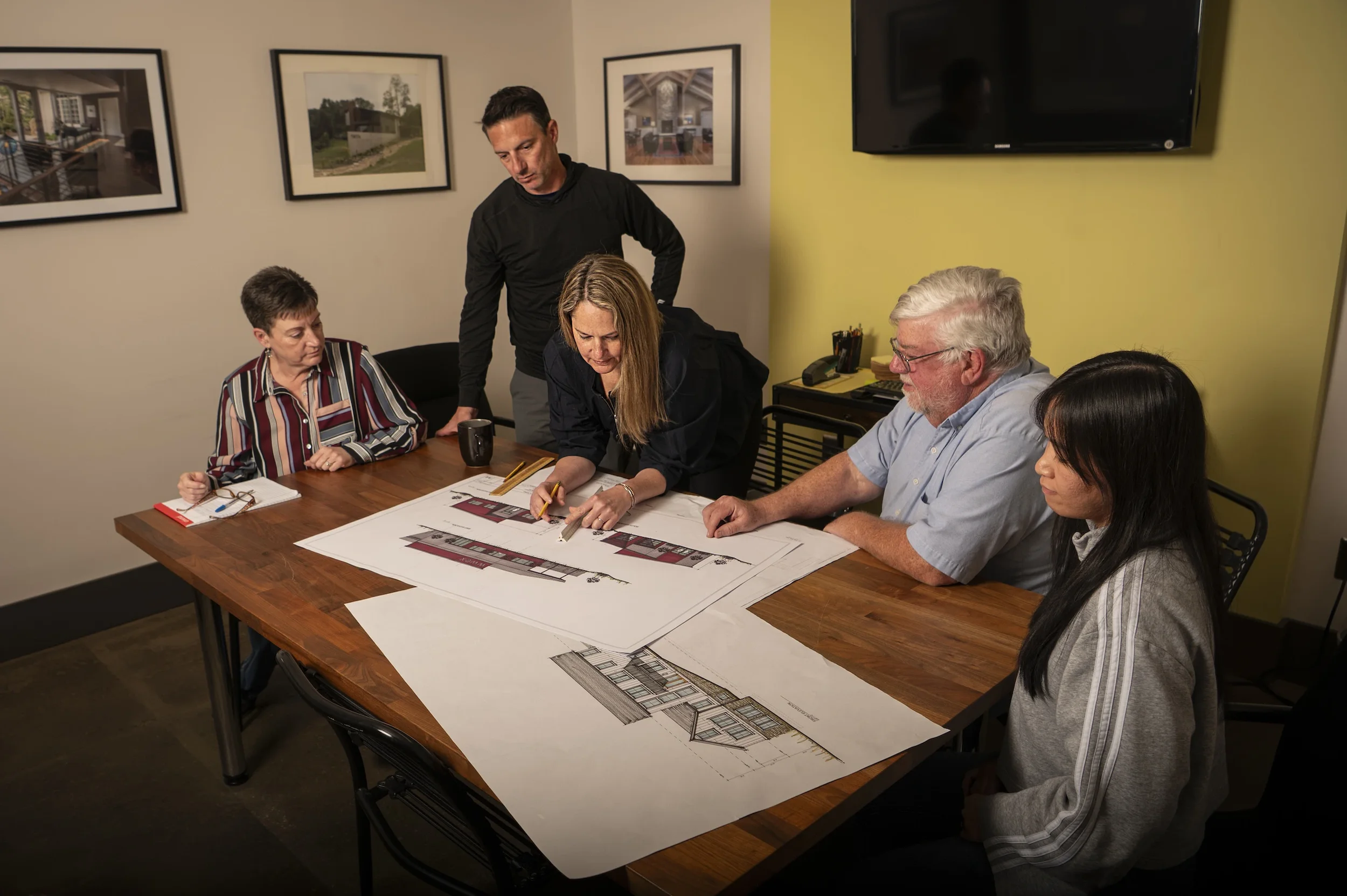 A group of five people working together at a table with architectural plans and drawings in a meeting room.