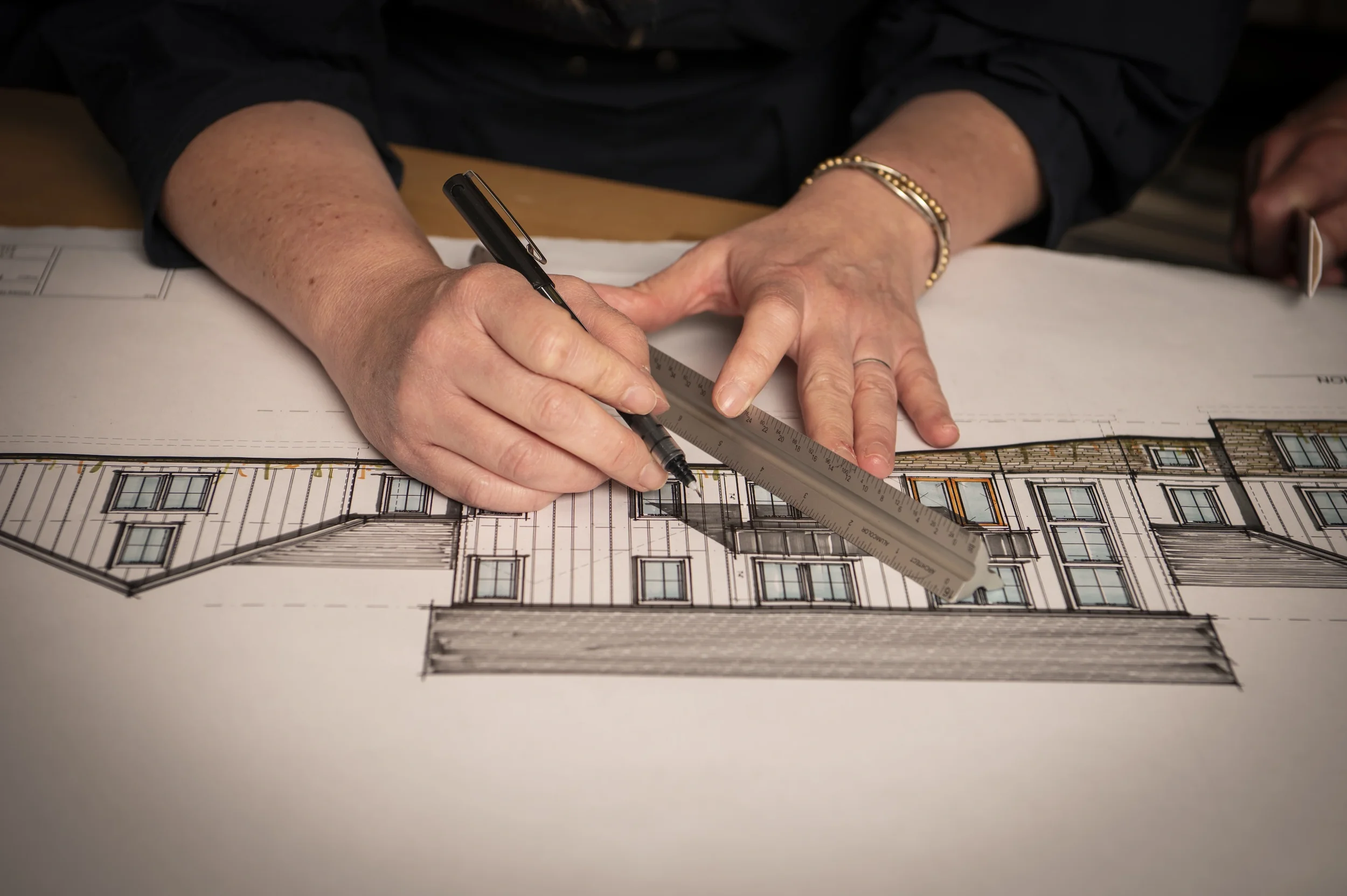 Close-up of a person's hands using a ruler and pen to examine an architectural blueprint of a building.
