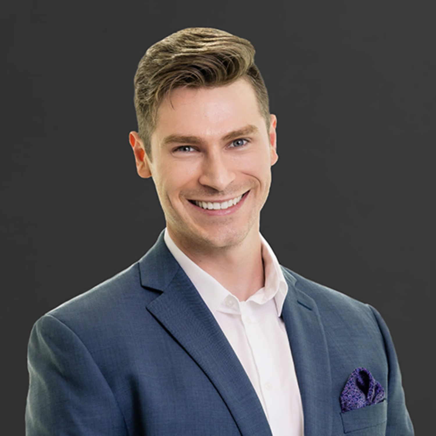 A smiling man in a blue suit with a white shirt and purple pocket square, posed against a dark background.