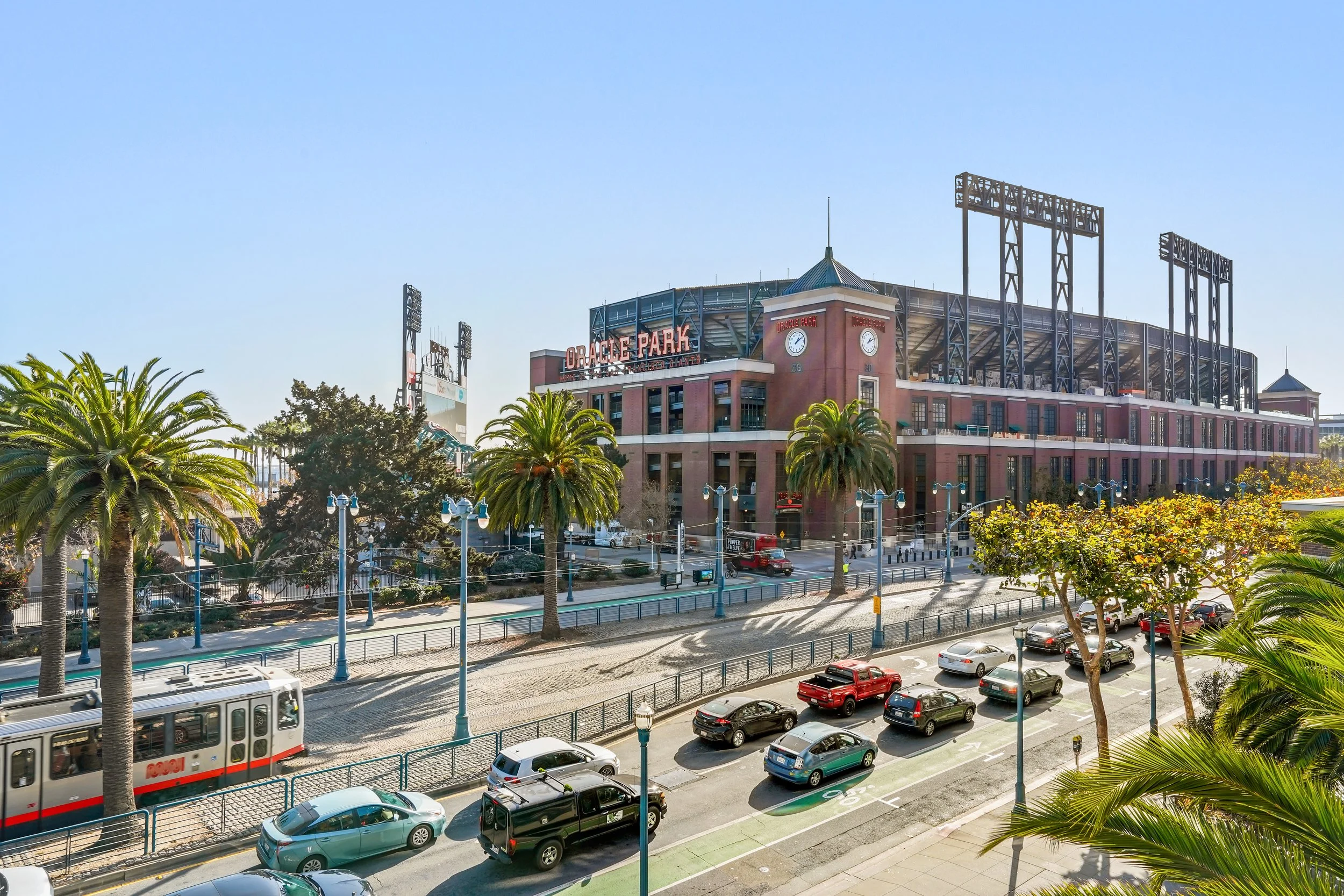San Francisco Giants baseball stadium, Oracle Park, with palm trees and parked cars in front on a sunny day.
