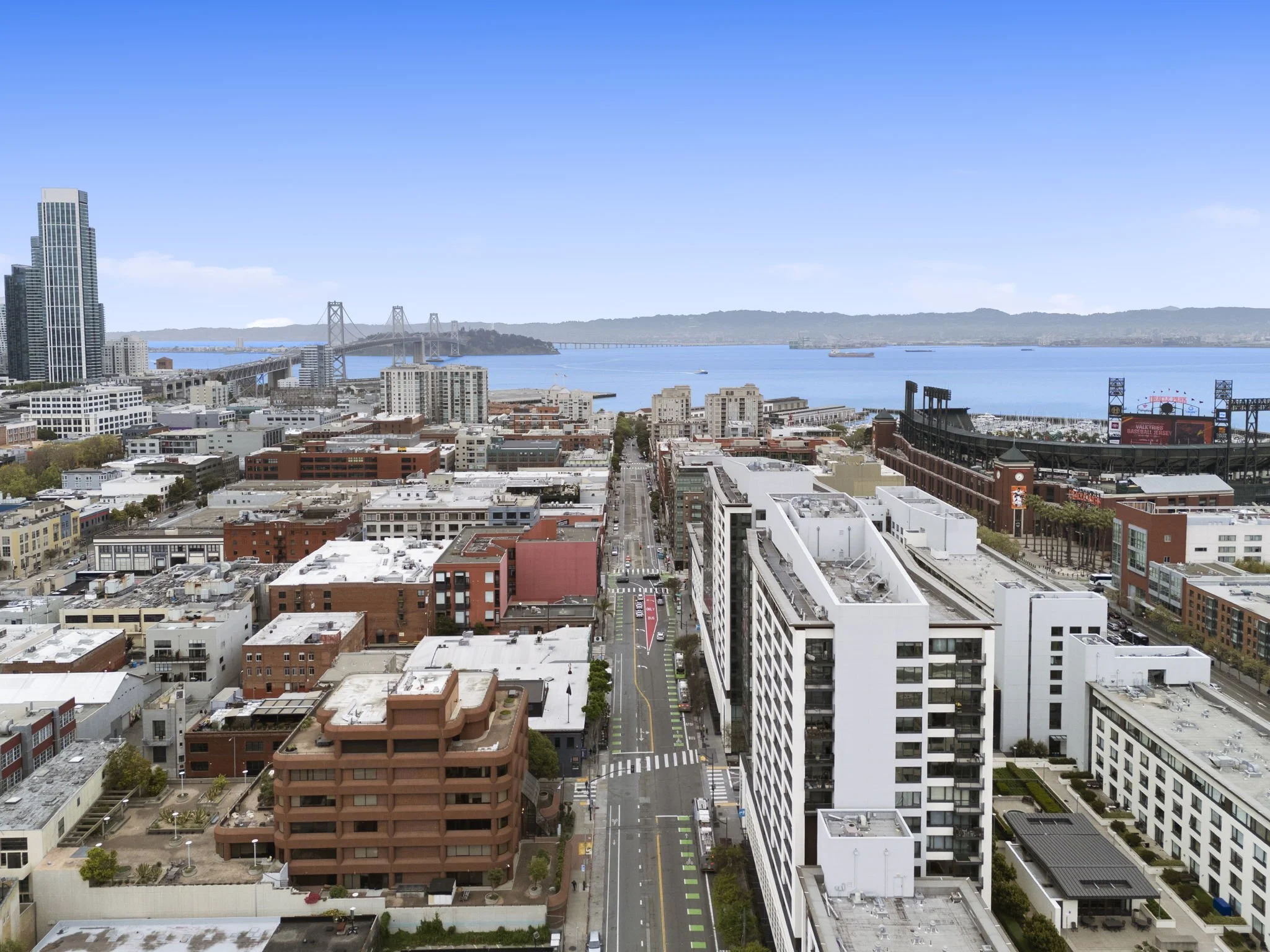 Aerial view of a cityscape near the bay with tall buildings, a bridge, and ships on the water during daytime.
