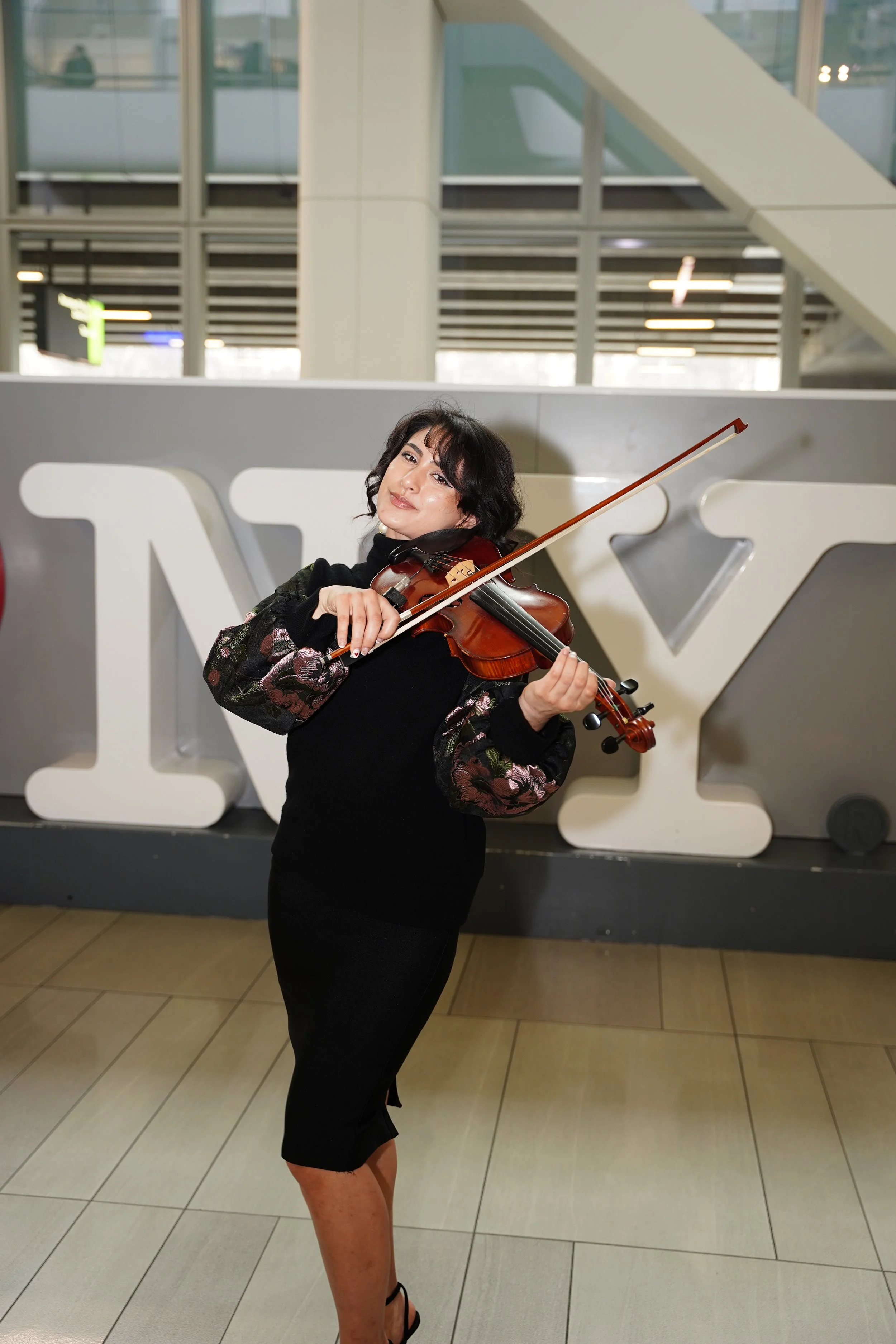 A woman in a black dress playing a violin indoors with a large white sculpture in the background.