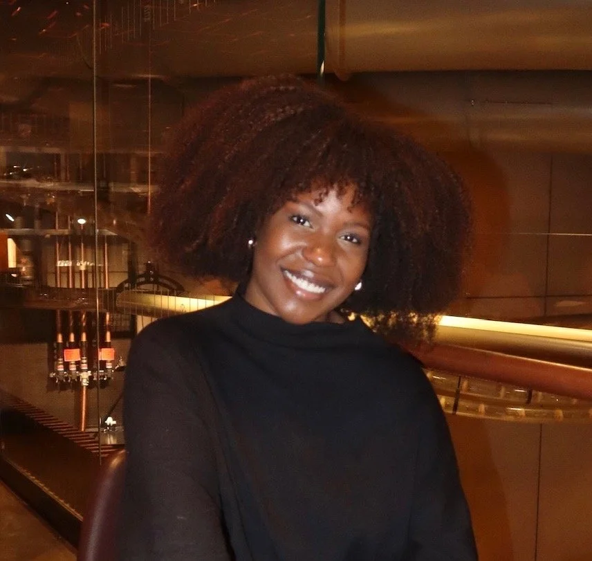 A woman with curly dark hair smiling in an indoor setting.