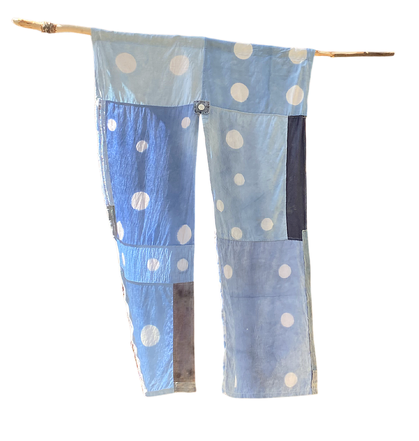 Clothing hanging on a wooden pole, including a light blue fabric with white polka dots and a dark gray section.