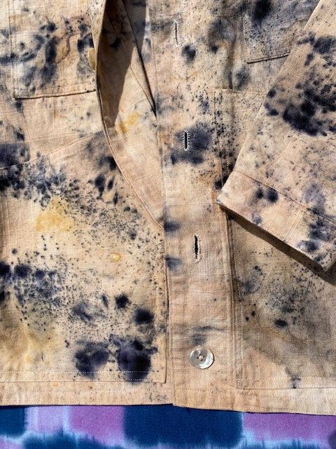 Close-up of a beige work shirt with black and yellow stains, metal buttons, and collar.