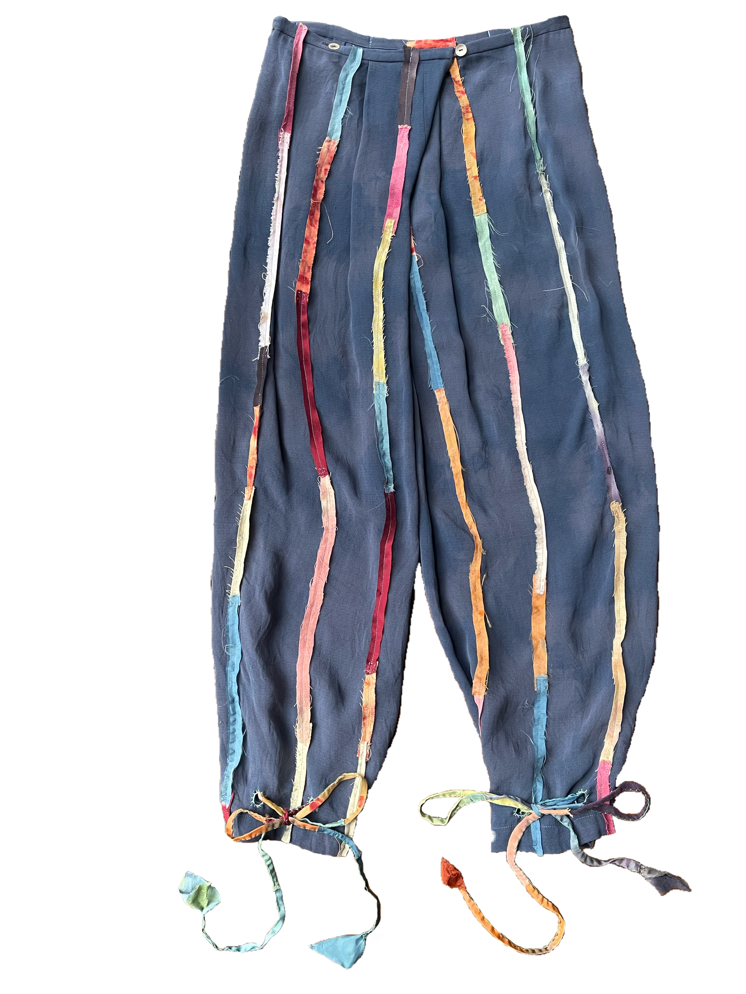 Pair of blue pants with colorful frayed fabric strips hanging from the waistband to the hem, tied in bows at the bottom and featuring white buttons on the waistband.