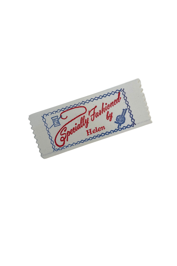 A fabric label with embroidered text that reads "Specially Fashioned by Helen," featuring sewing icons of a needle and thread and a ball of yarn within a decorative border.