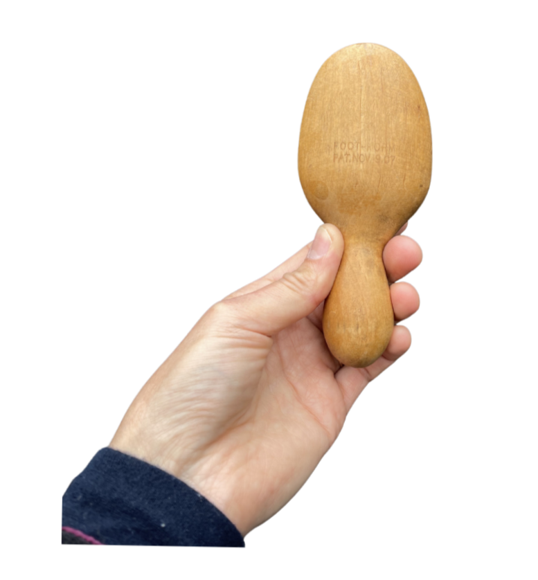 A person holding a wooden meat tenderizer with a round top and handle against a white background.
