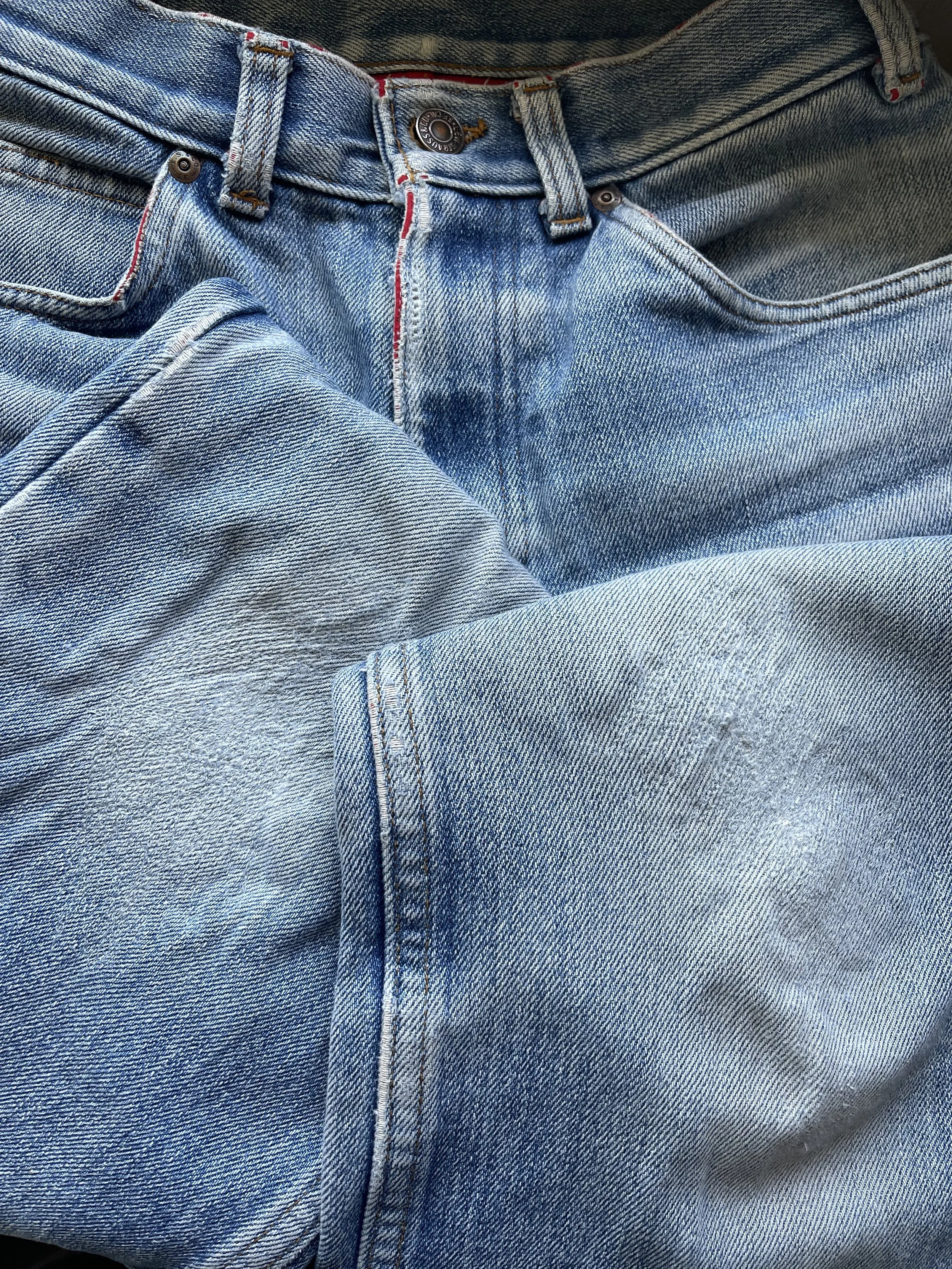 Close-up of blue denim jeans showing the waistband, belt loops, and zipper area with detailed stitching.