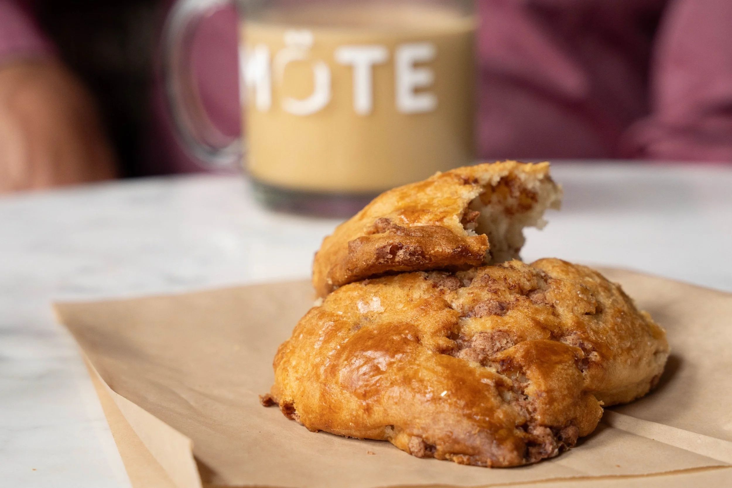 Close-up of two golden brown scones with Möte coffee mug in the background, slightly out of focus.