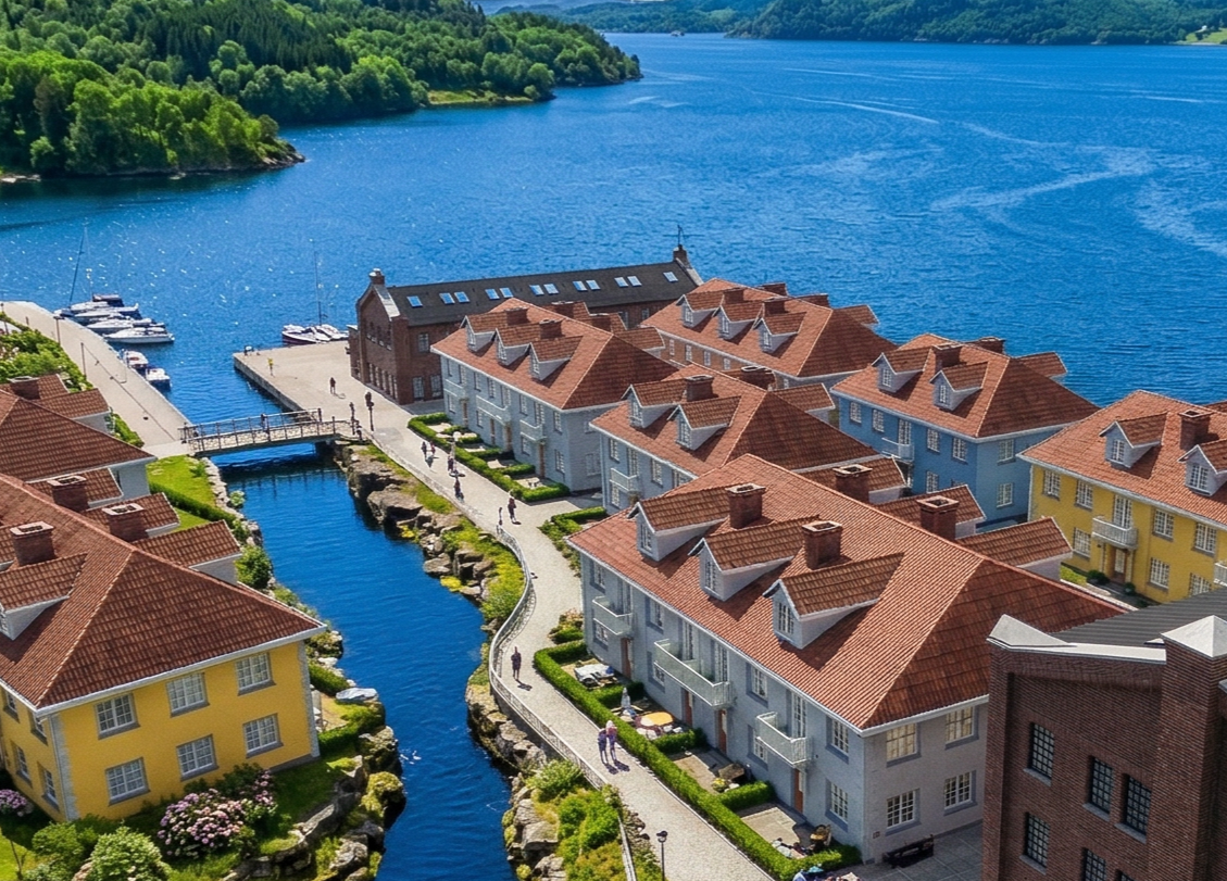 A picturesque waterfront town with colorful buildings, a canal, and a large lake in the background.