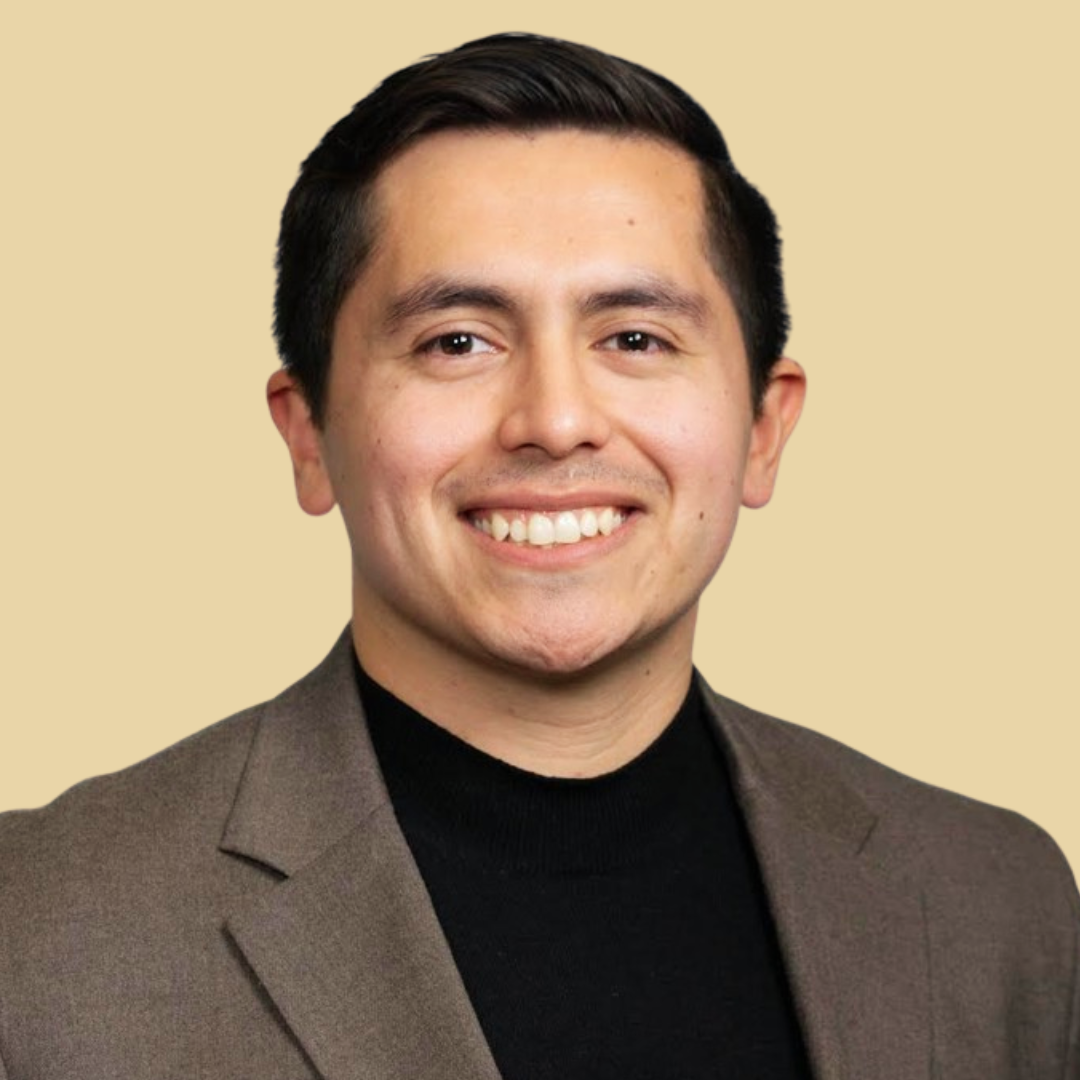 Headshot of smiling male consultant with short black hair wearing a brown blazer.