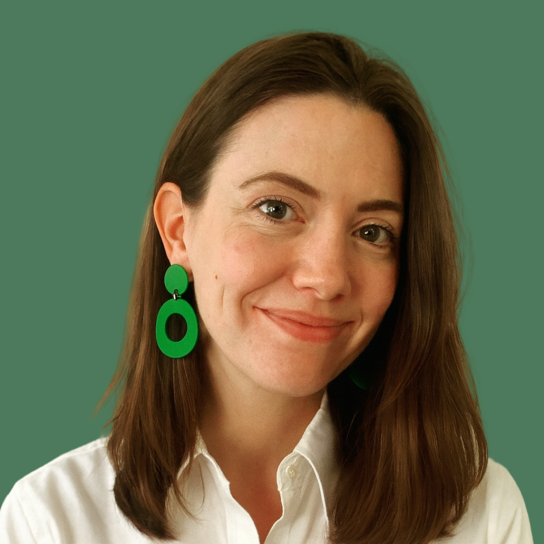 Headshot of smiling female consultant with long brown hair wearing a white shirt and green earrings..