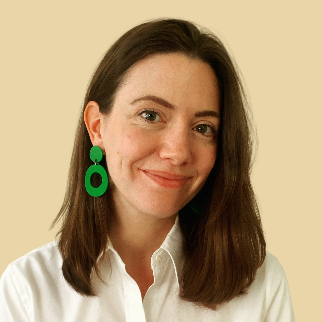 Headshot of smiling female consultant with long brown hair wearing a white shirt and green earrings..