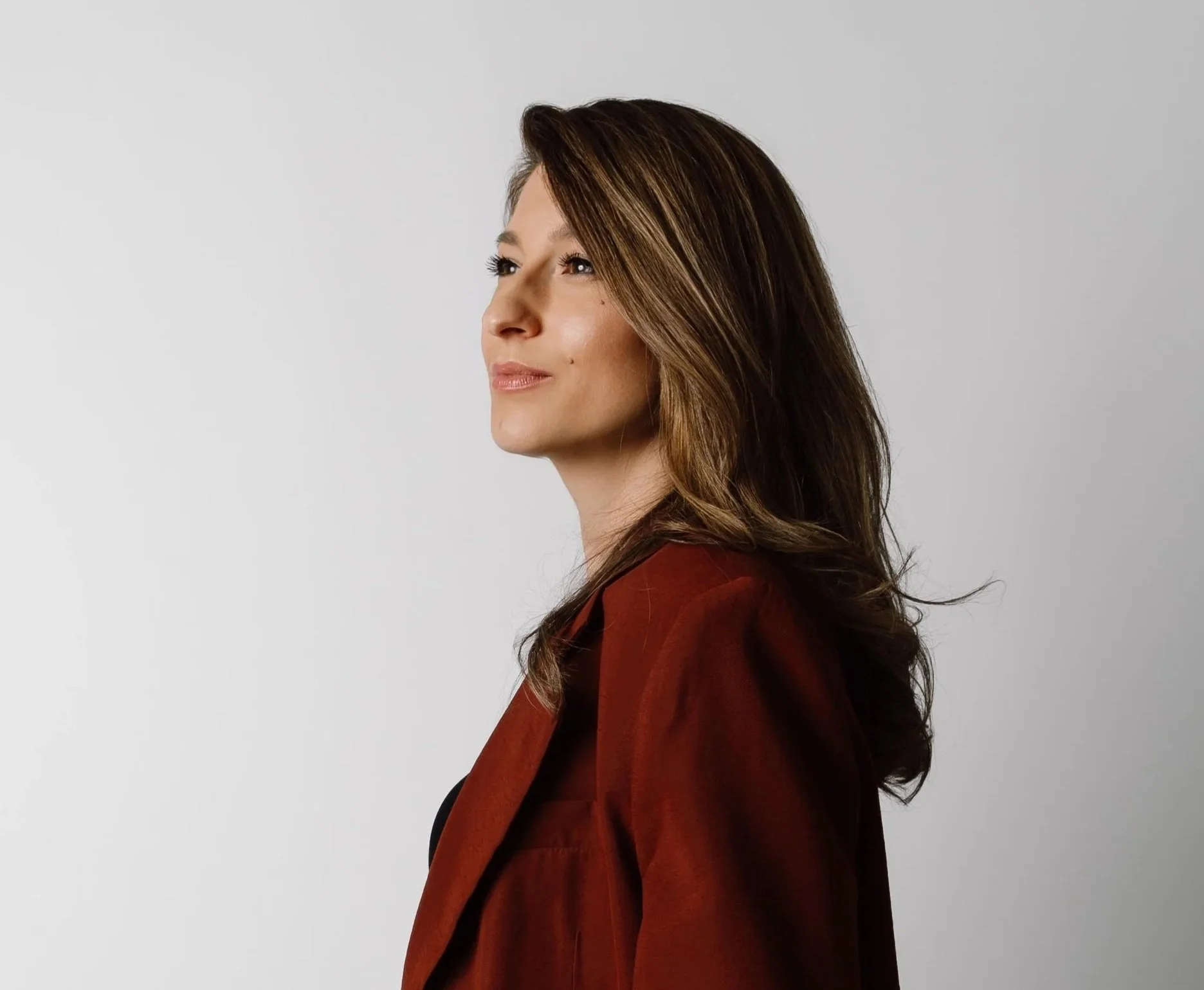 Portrait of a woman with long brown hair wearing a dark red blazer, looking slightly upward, representing a forward-looking approach to human–AI collaboration and organizational change