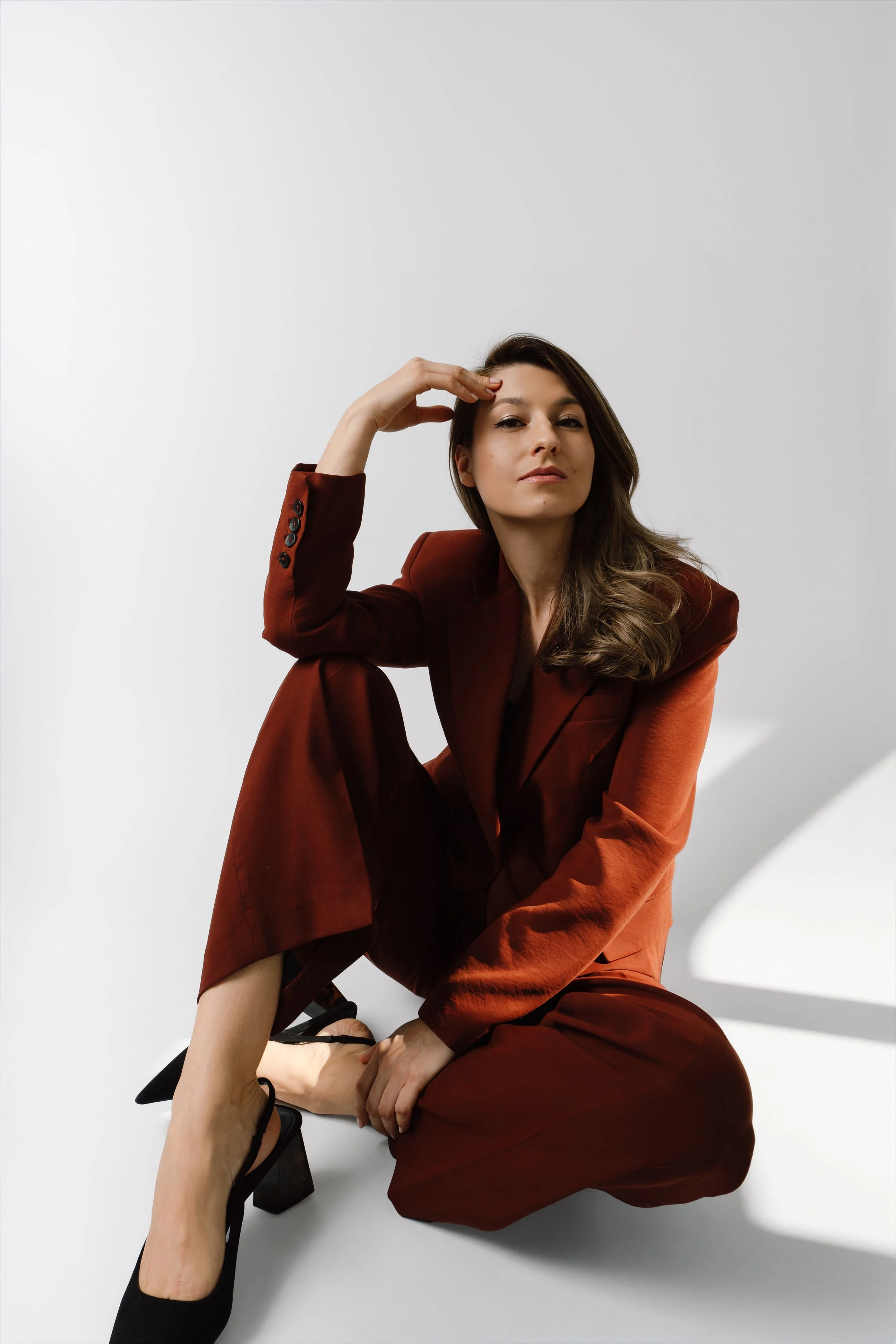 Woman in a rust-colored suit sitting on the floor with hand on forehead, expressing reflection and decision-making in the context of AI adoption and change.