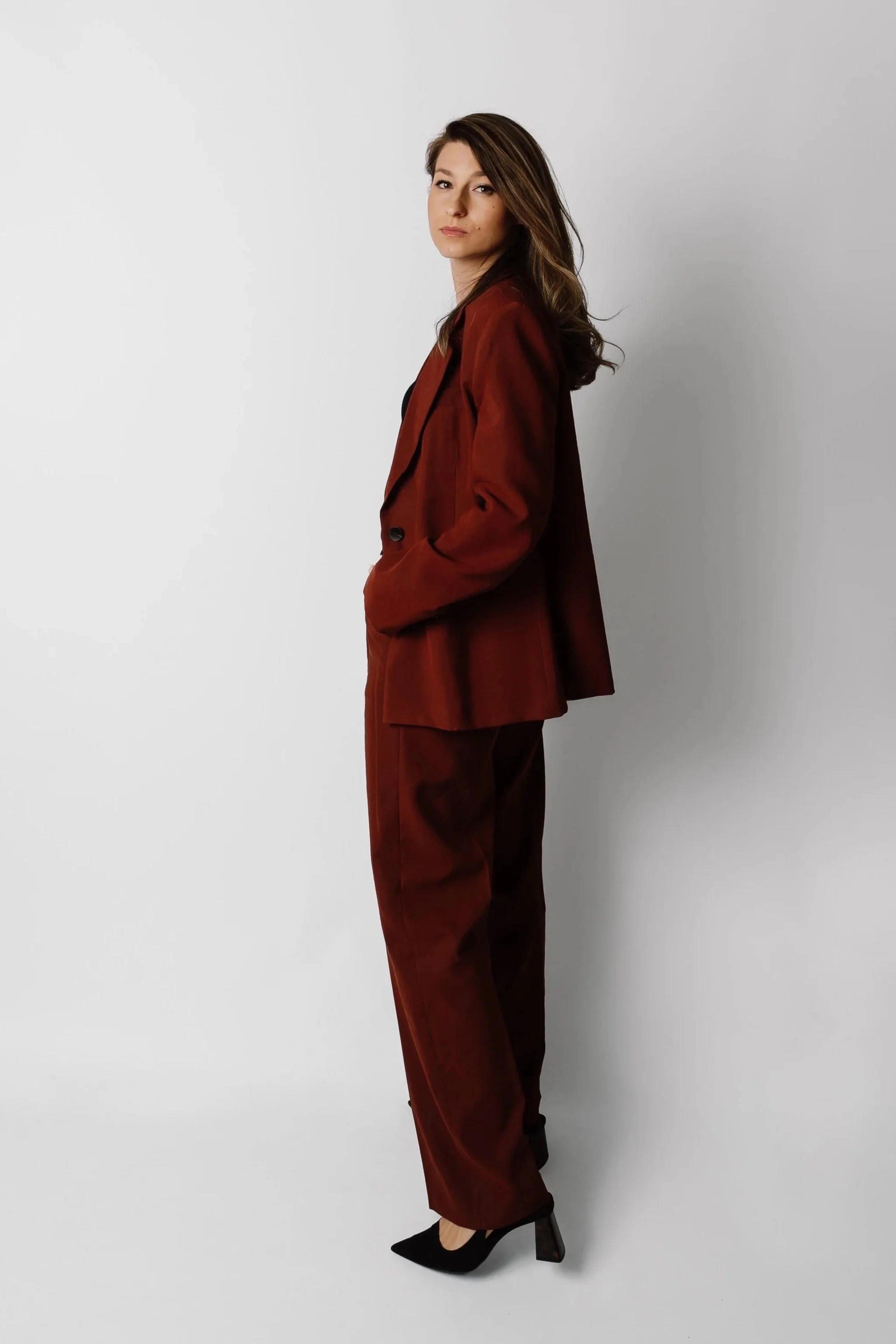 Woman in a rust-colored suit standing confidently with hands in pockets, representing a structured approach to AI adoption and transformation.