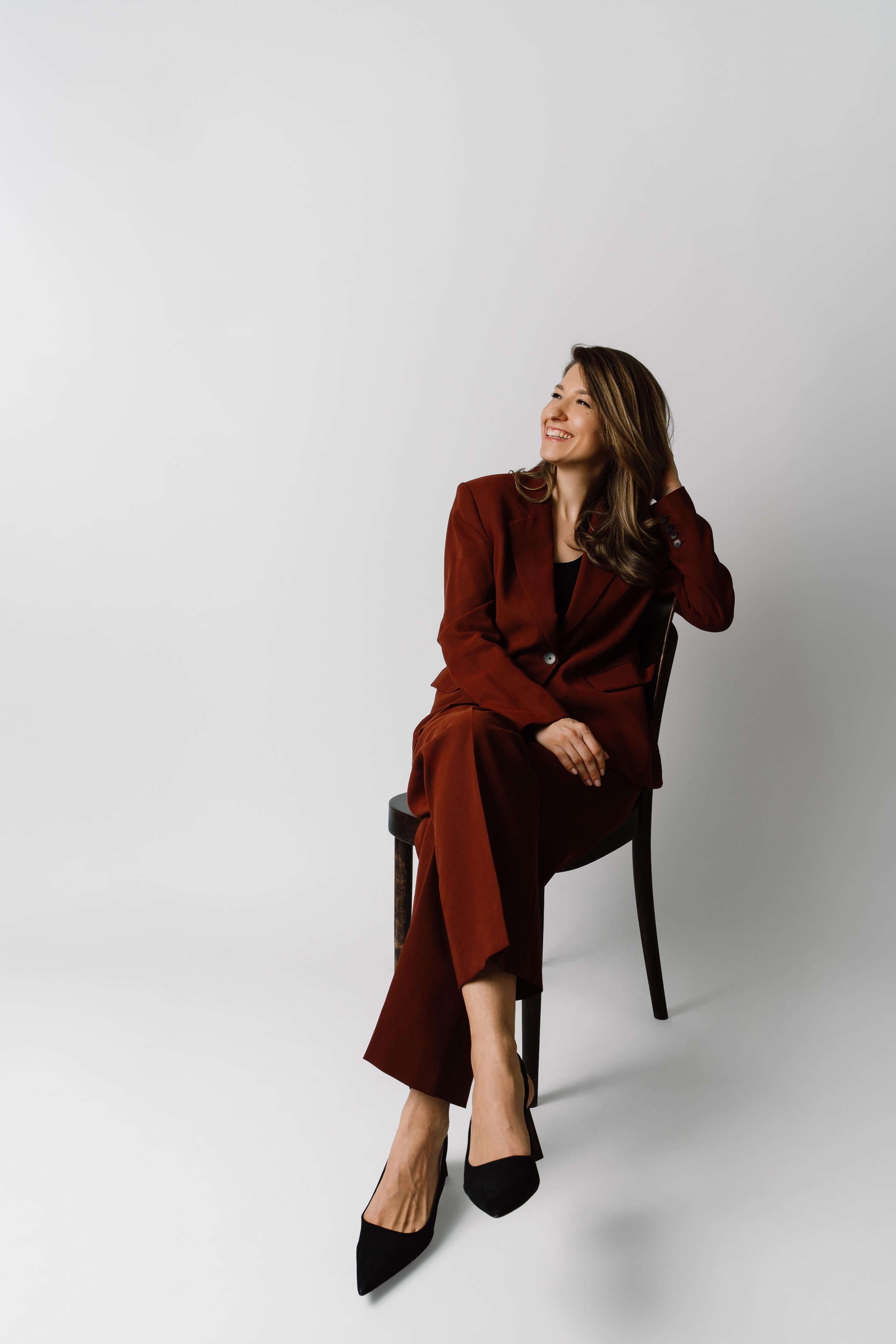 Woman with long wavy brown hair sitting on a black chair, smiling, representing a human-centered approach to AI and organizational change.