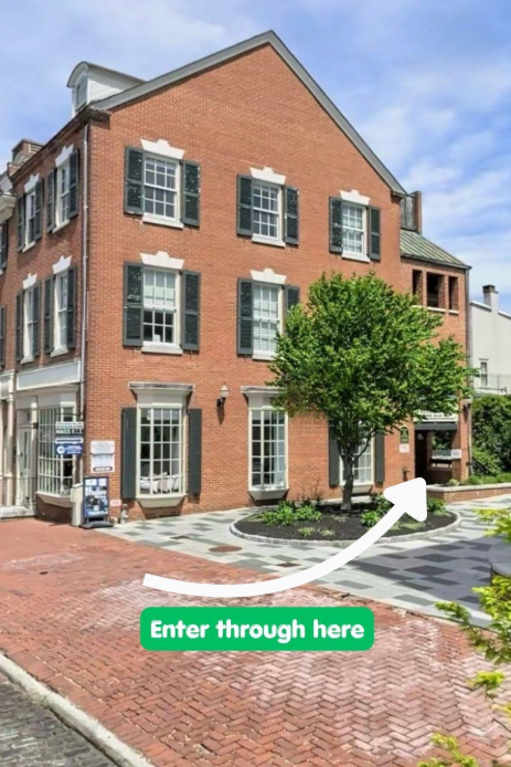 A three-story brick building with black shutters, a small tree in front, and a sign pointing to an entrance with the text "Enter through here." Vérité Aesthetic Medicine | Injectables in Philadelphia