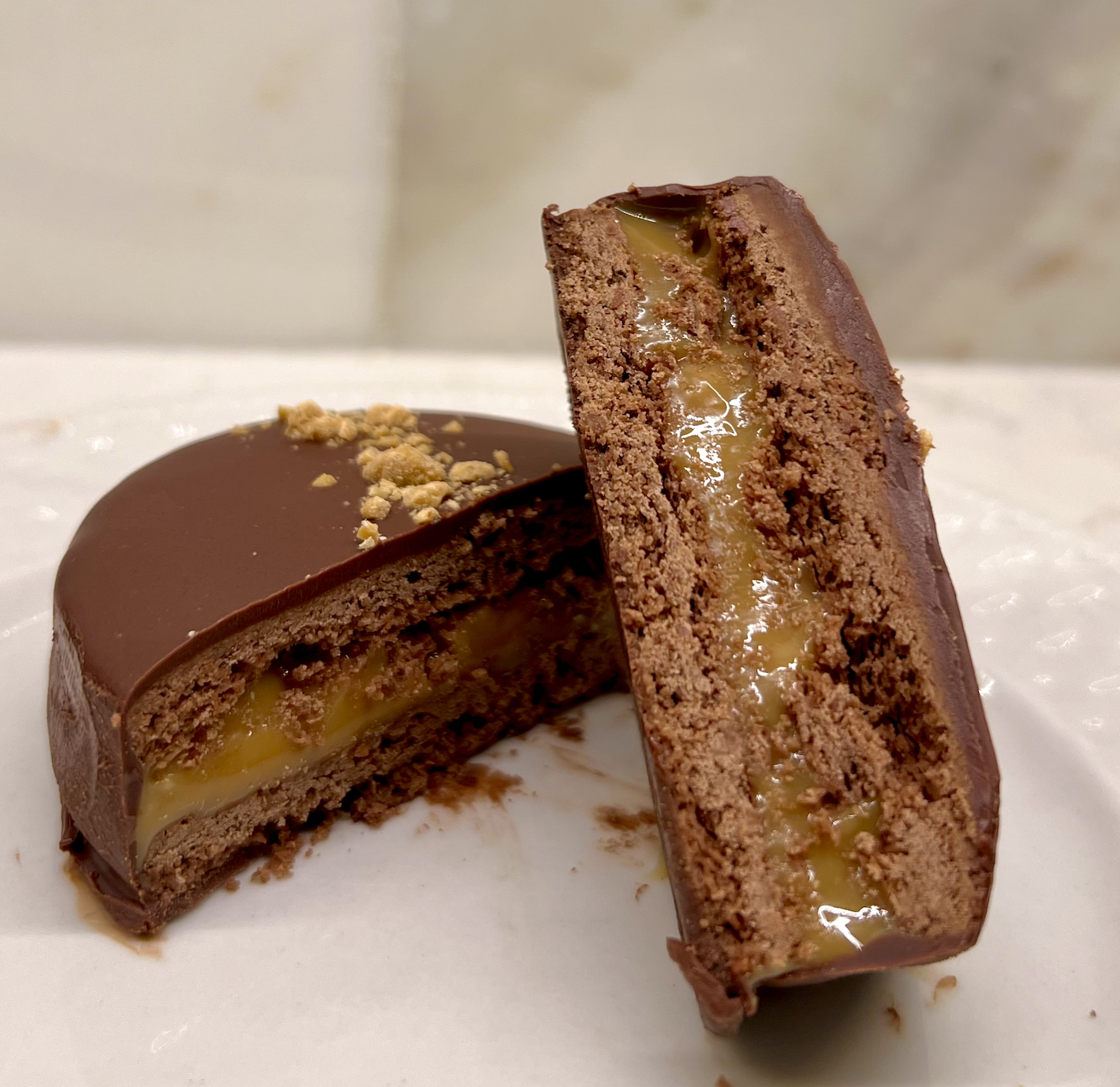 A chocolate dessert with a layer of caramel filling inside, topped with chopped nuts.
