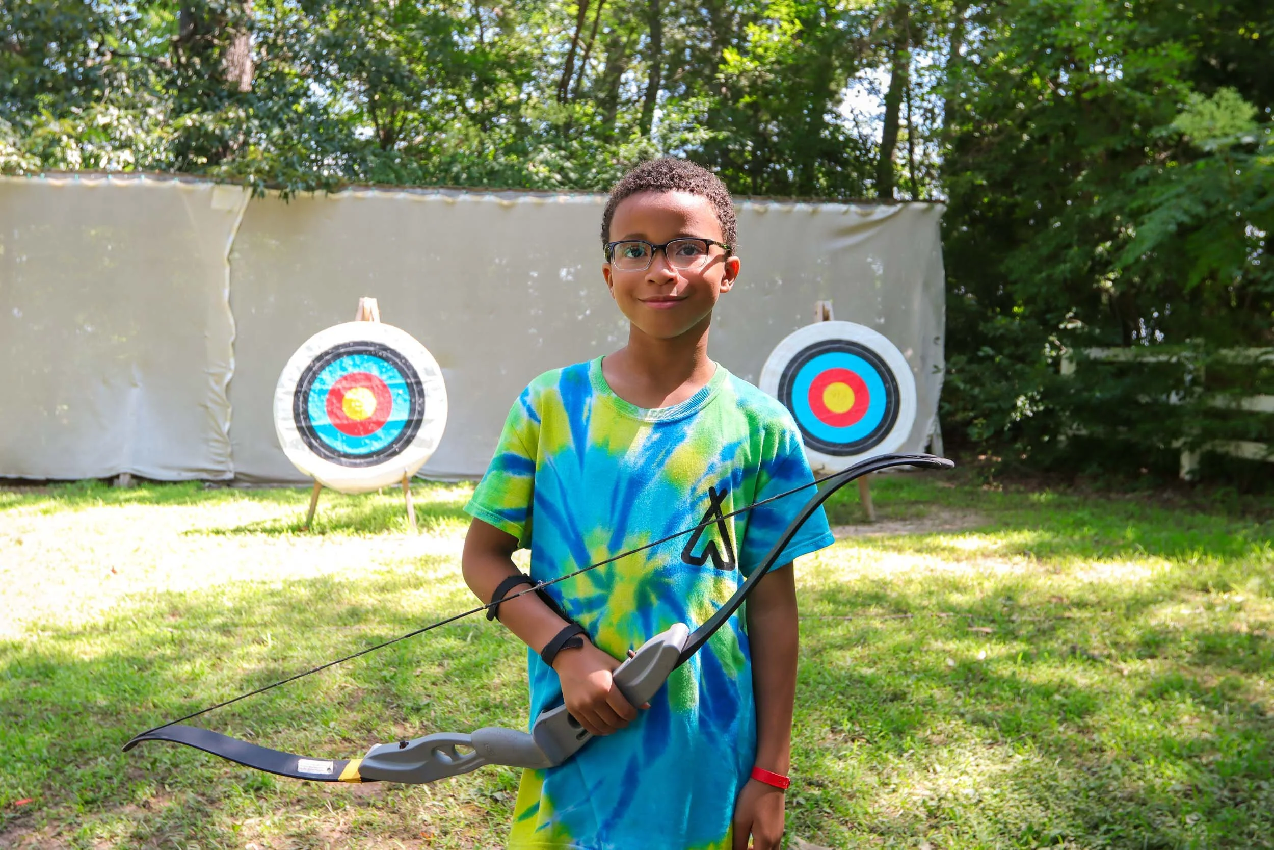 A young boy holds a bow at outdoor archery range.