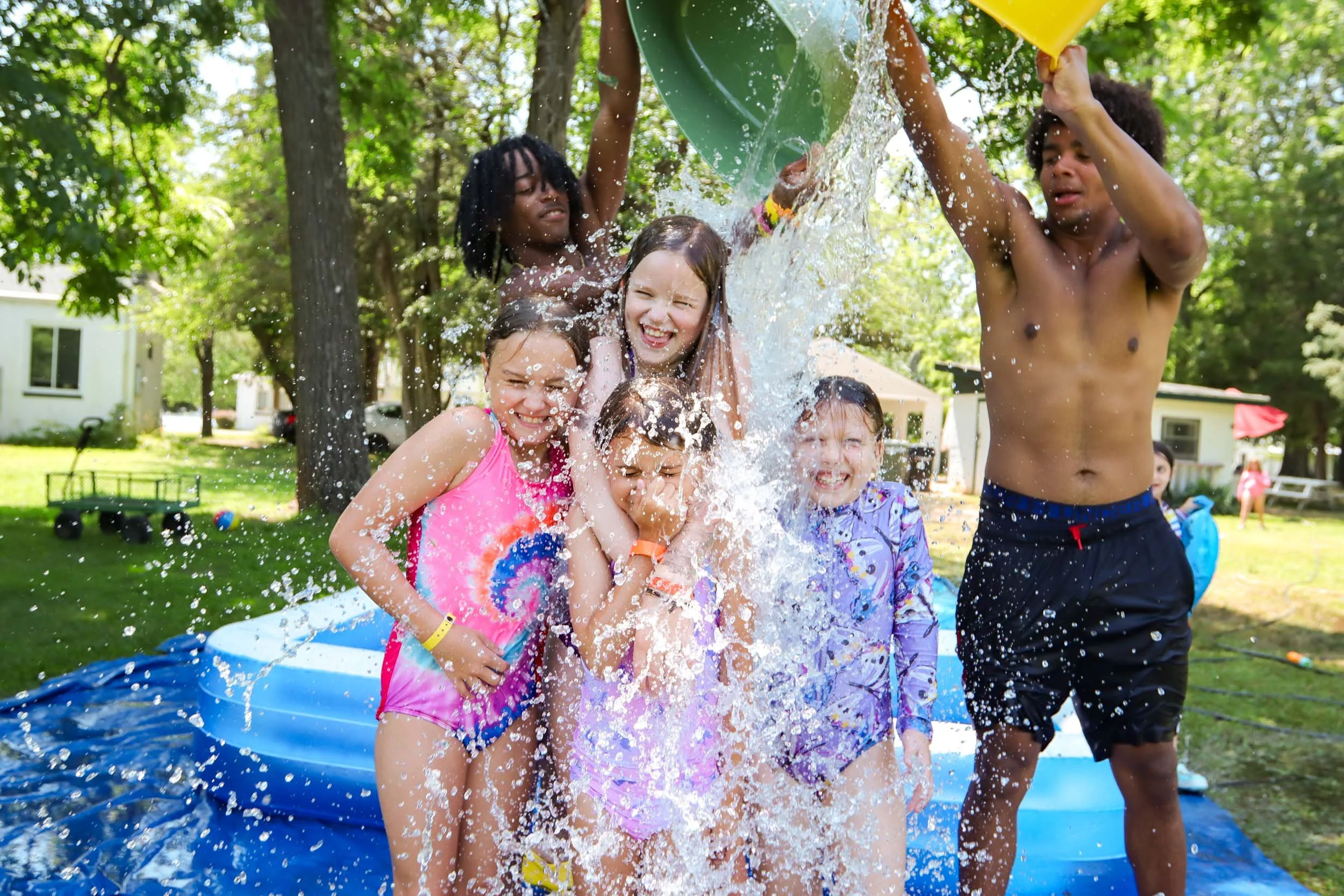 Two counselors dump water on a group of laughing girls.