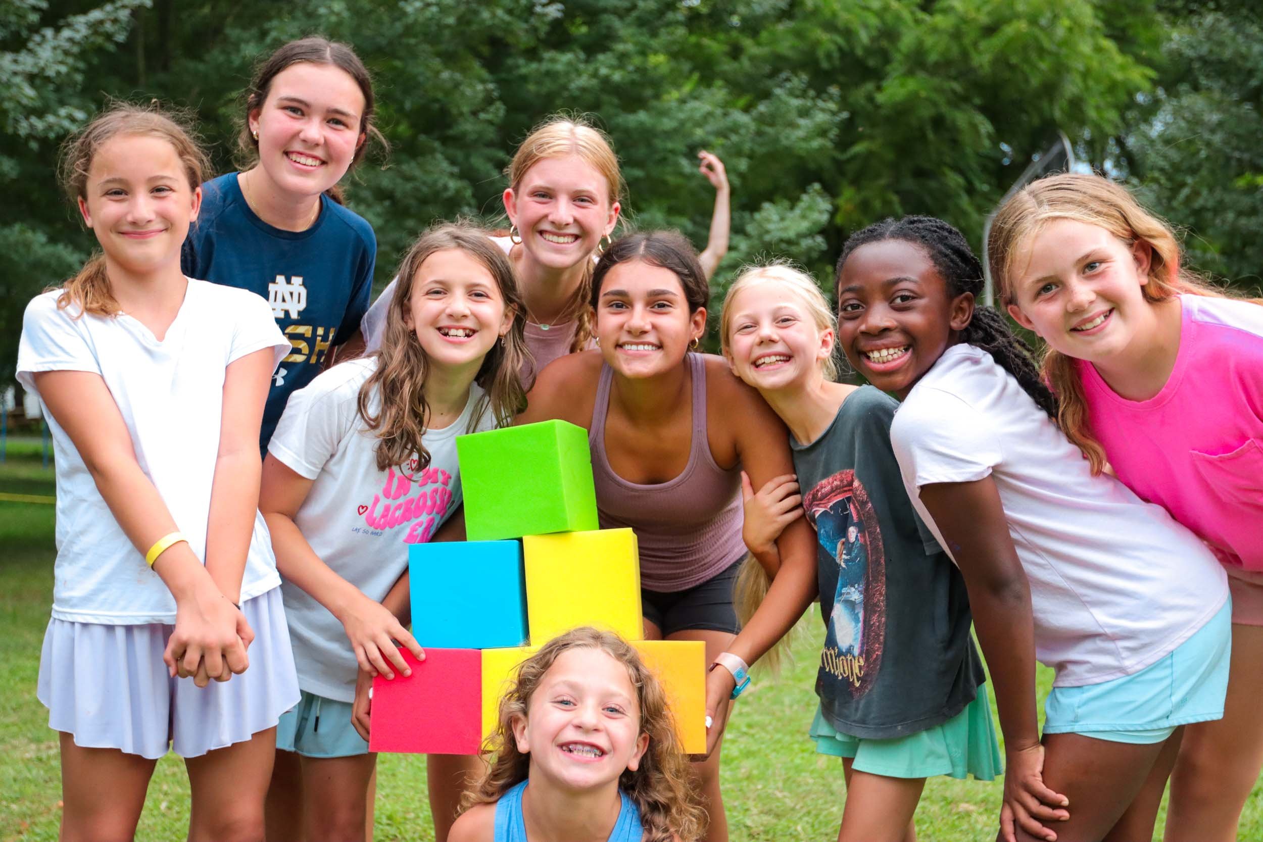 A group of smiling girls posing with a stack of colorful blocks.