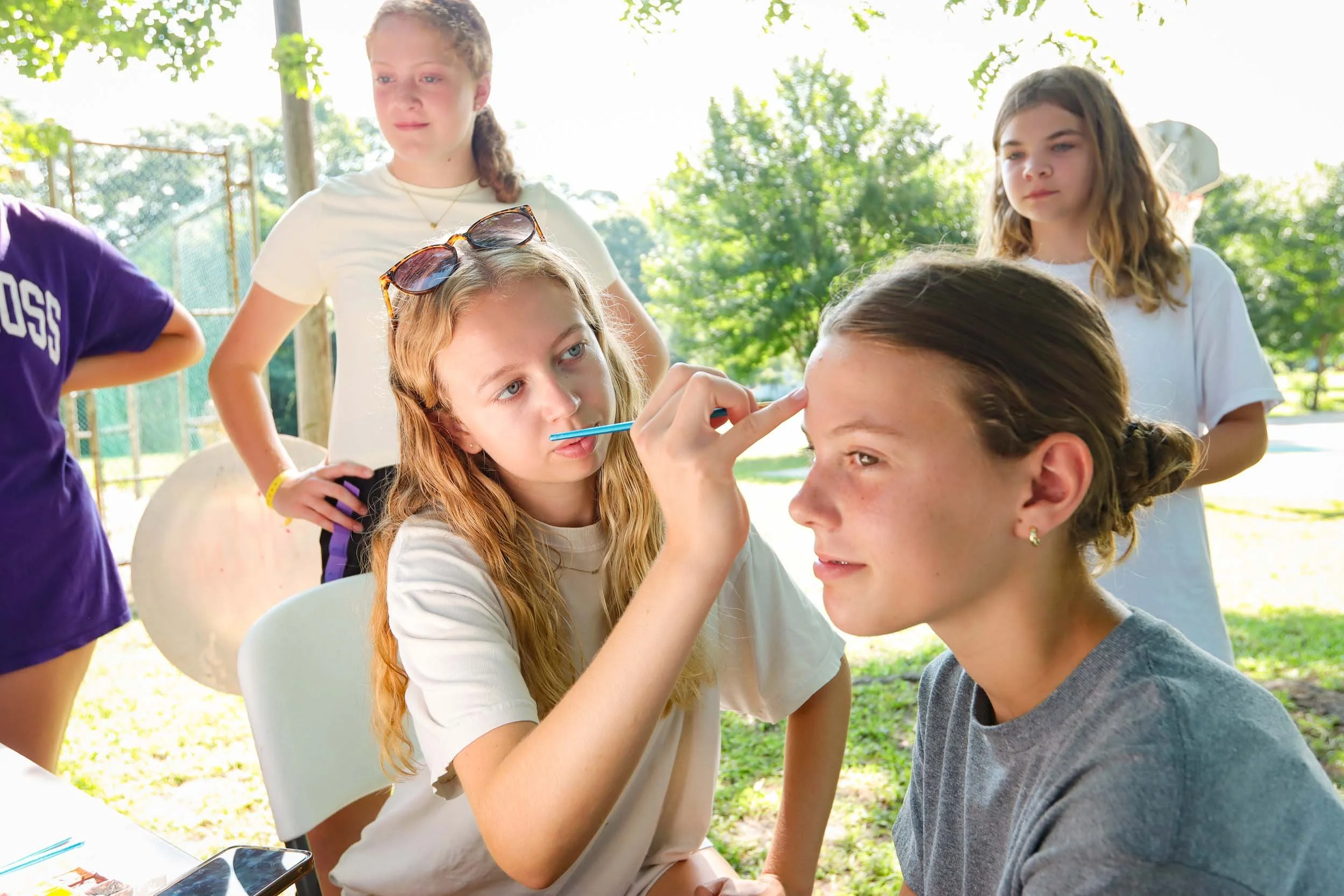 A camp counselor painting on a smiling campers face.