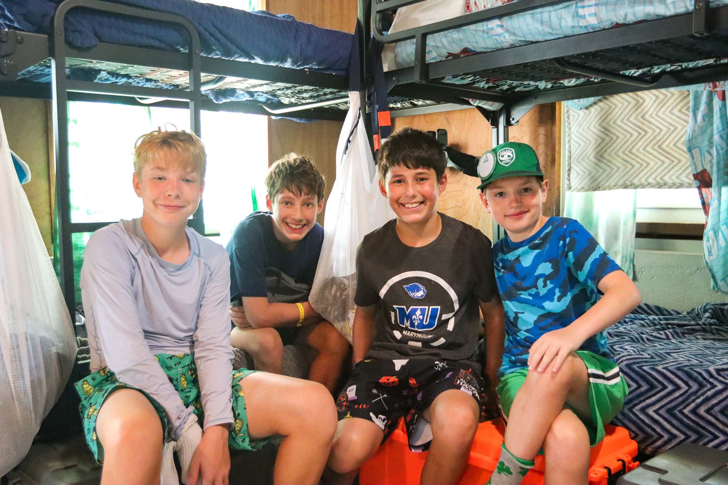 Four boys sitting in a bunk beds in their cabin, smiling at the camera.