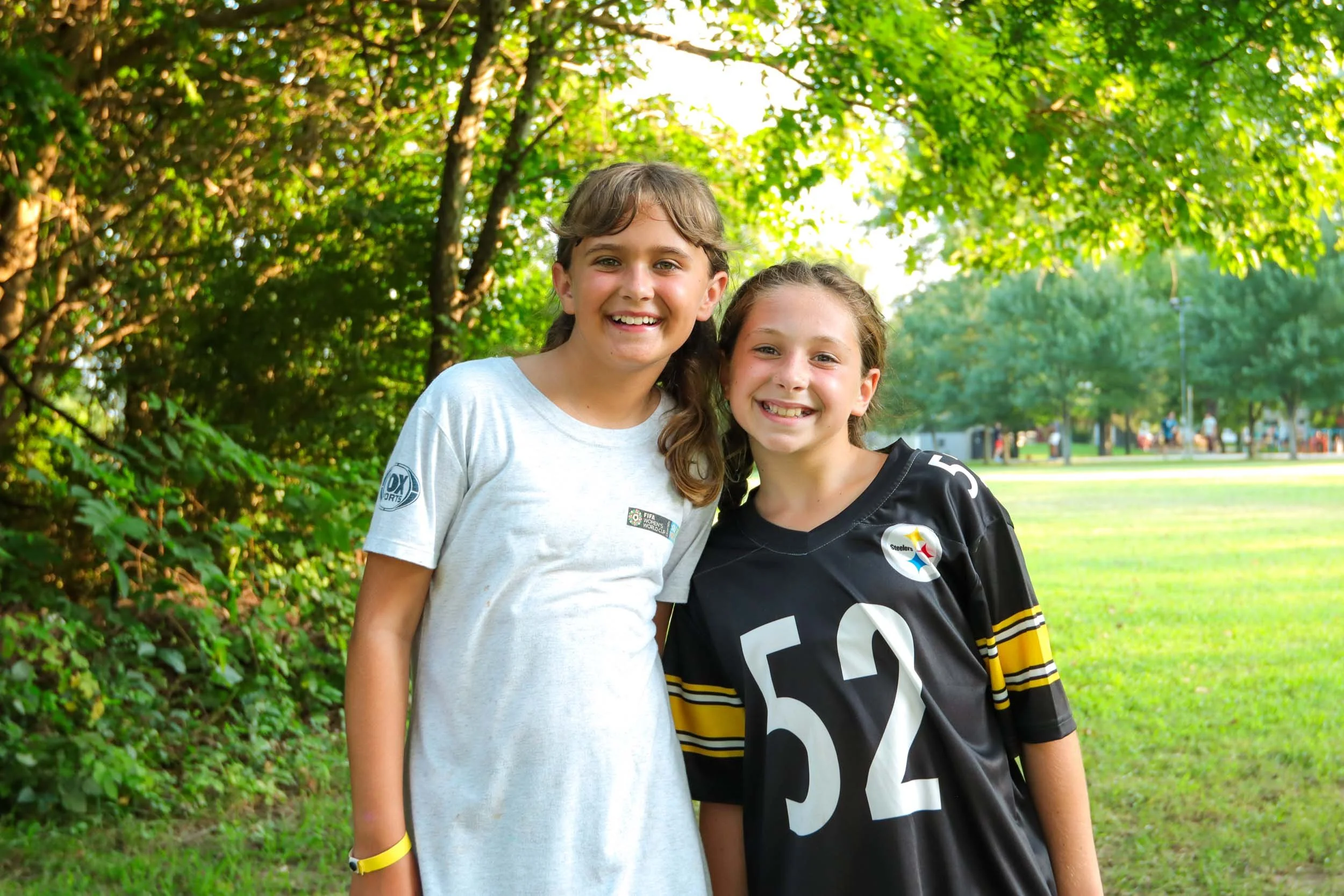 Two young girls smiling outdoors at camp.