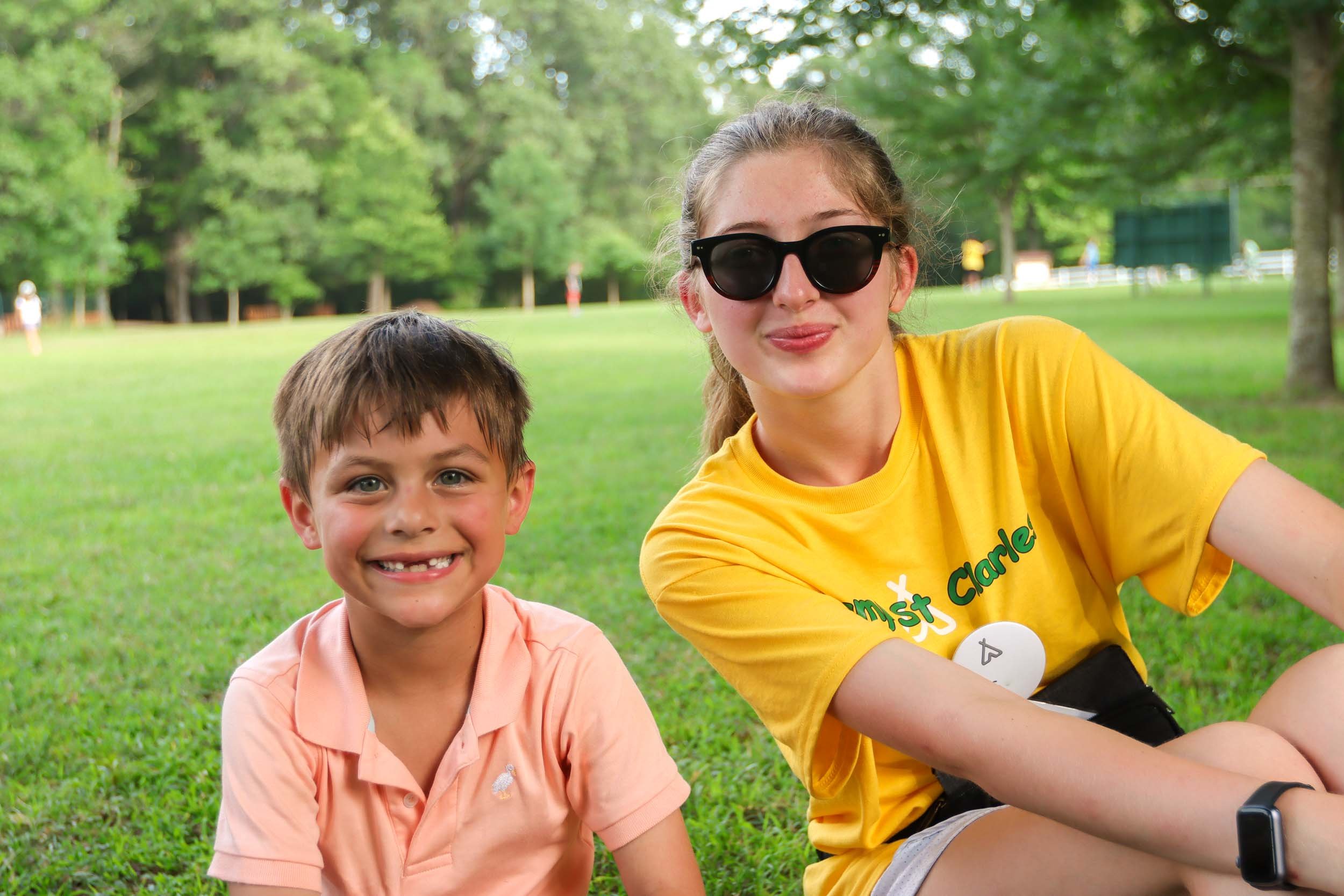 A young boy and a female counselor sitting on grass together.