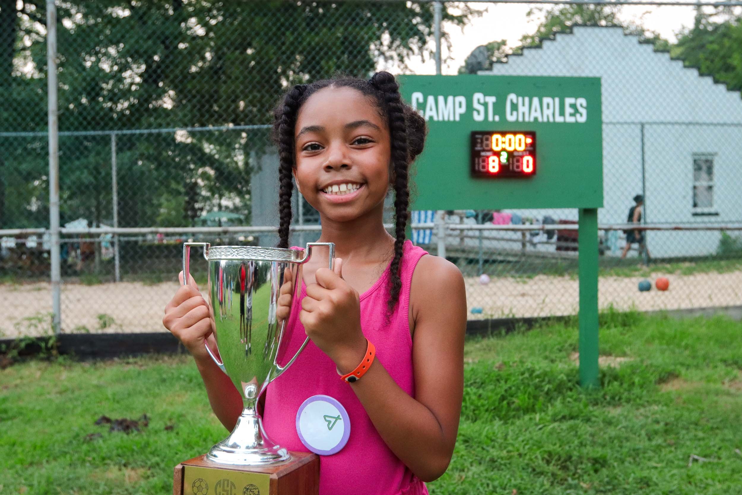 A young girl smiling and holding a trophy at a sports field.