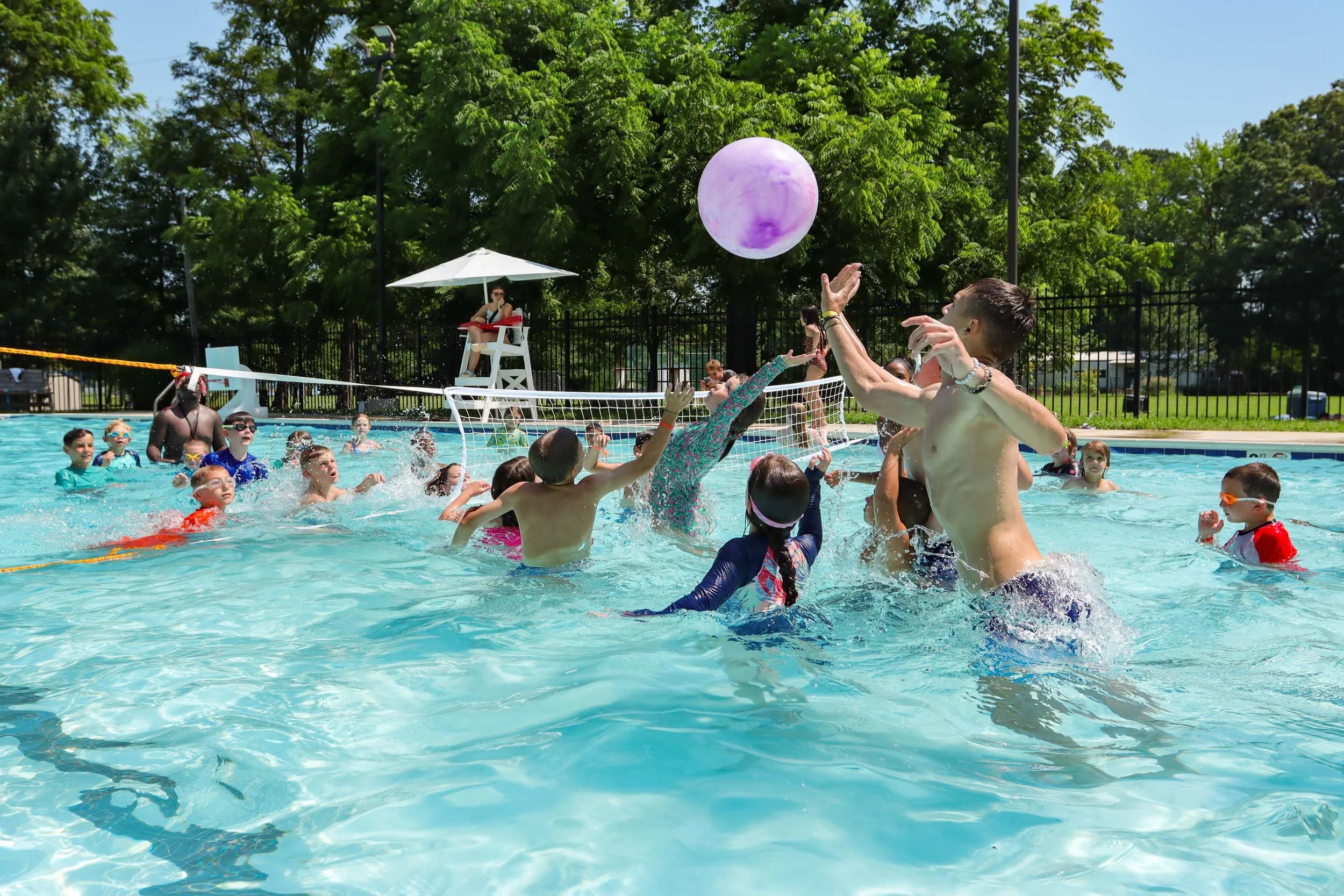 Campers and counselors playing water volleyball in an outdoor swimming pool.