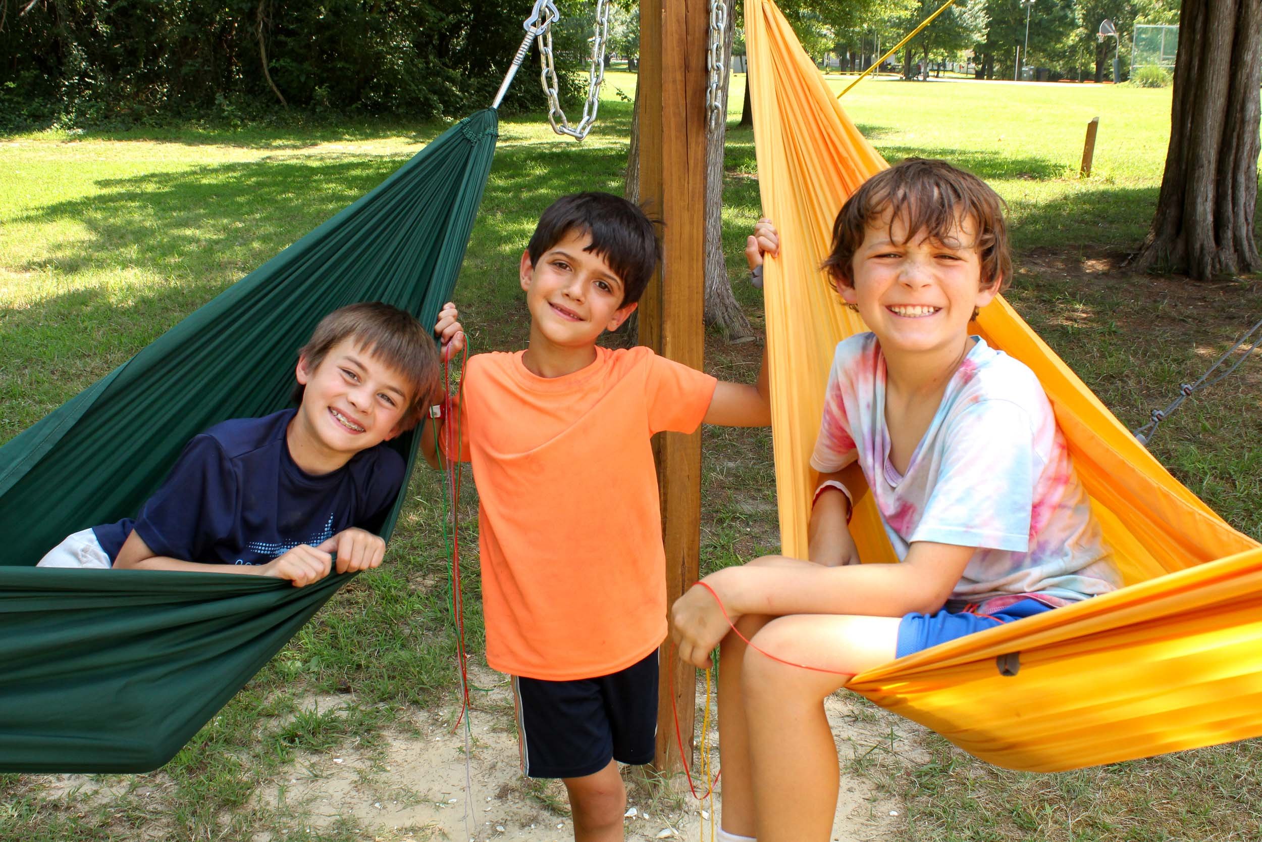 Three smiling boys sitting in colorful hammocks.