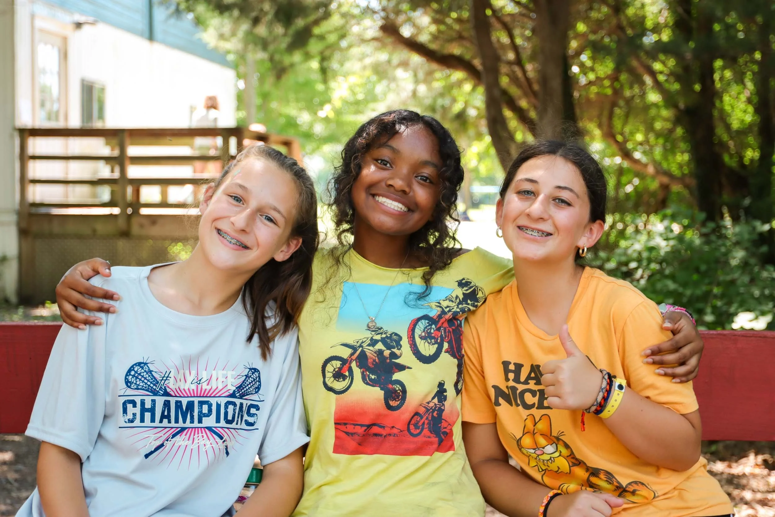 Three smiling girls sitting close together outdoors.