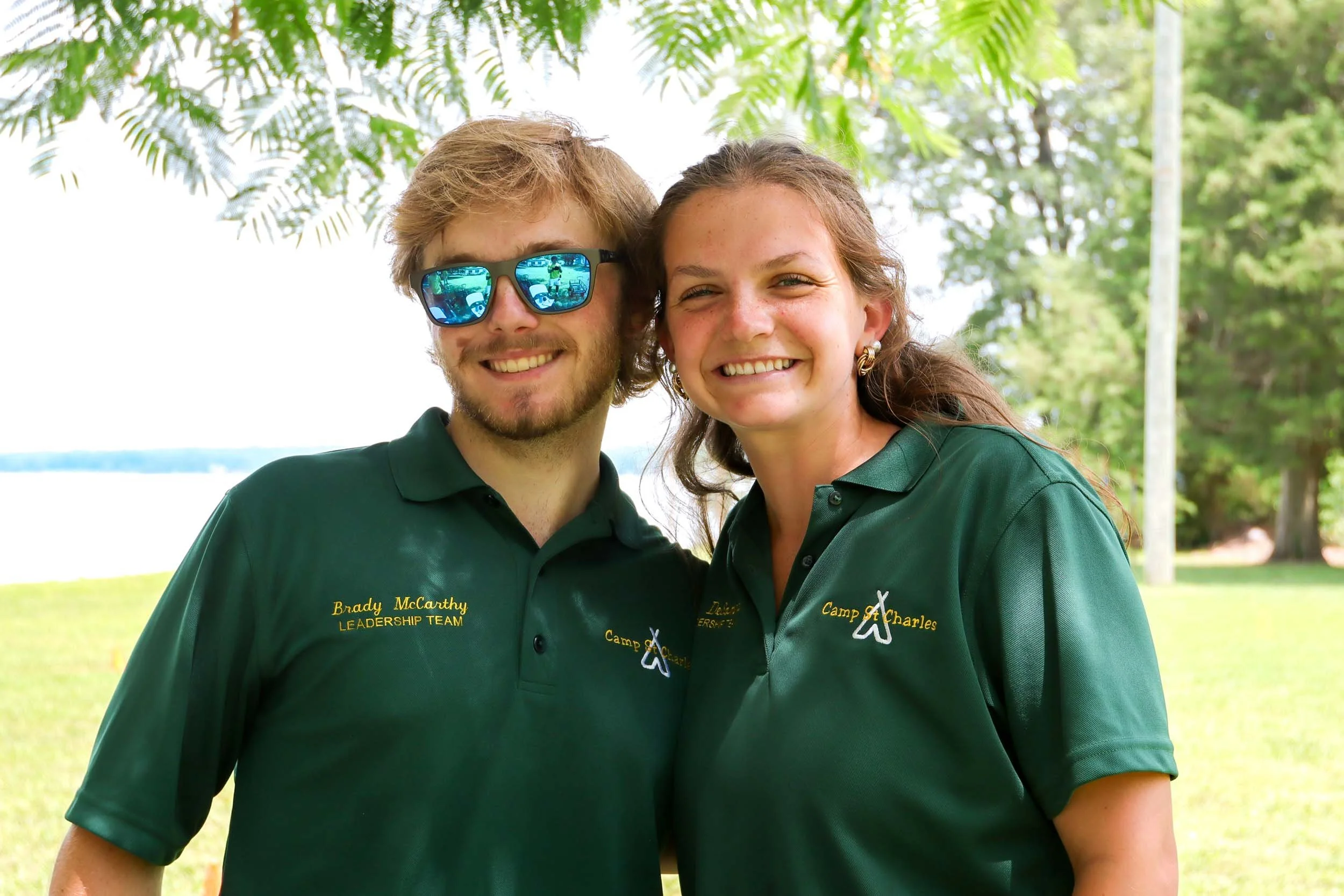 Two leadership staff smiling outdoors under green trees.
