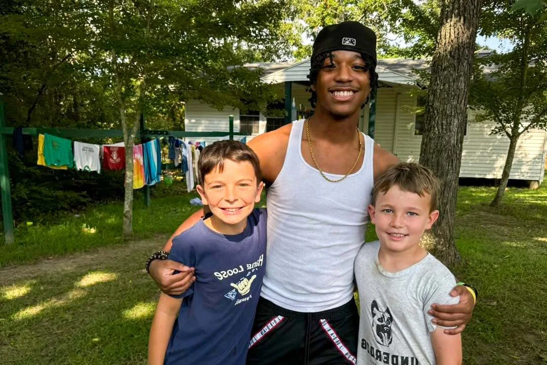 	
A camp counselor his two campers smiling and hugging outside their cabin.