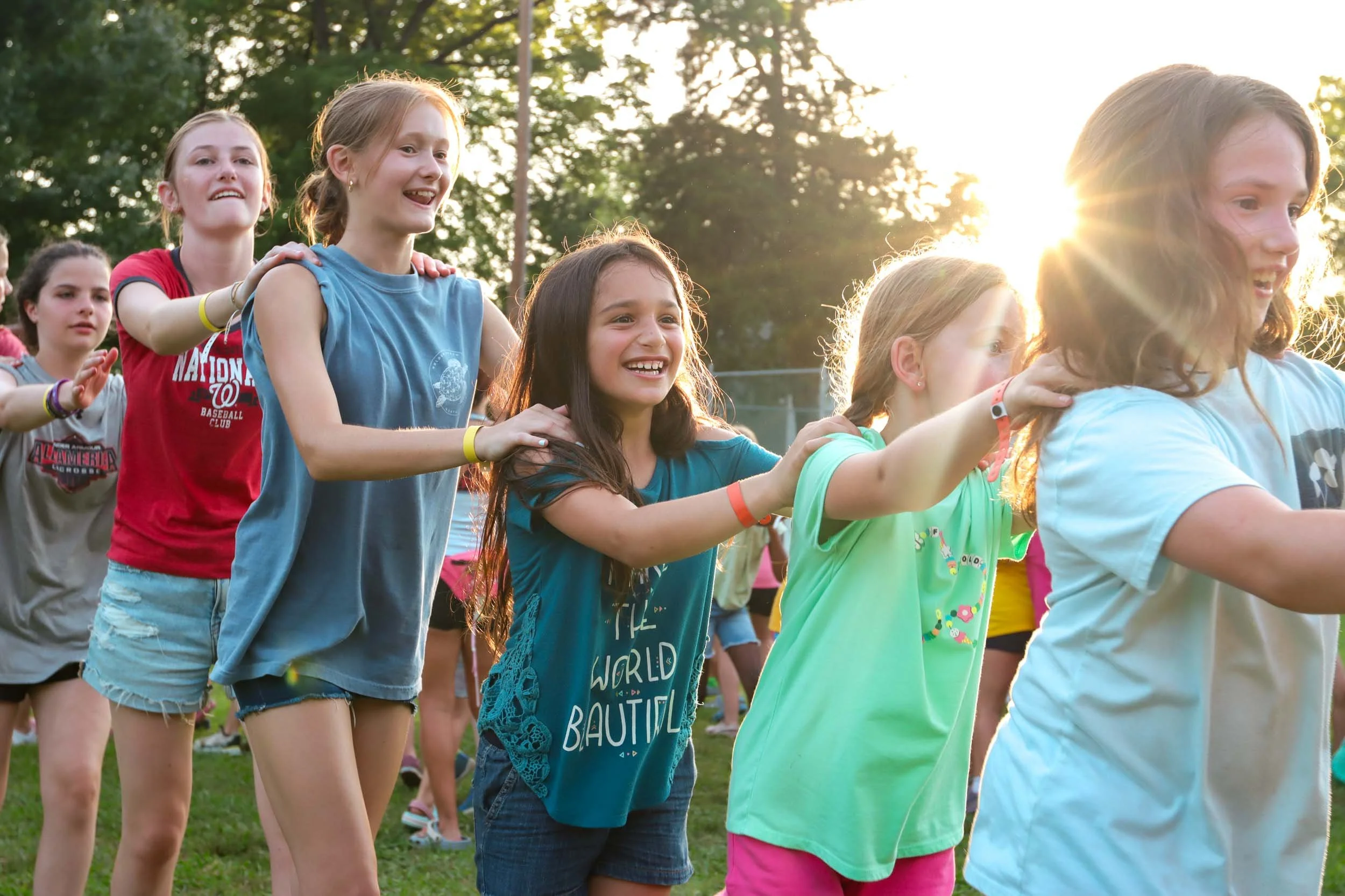Group of young girls holding onto each other's shoulders, smiling and laughing.