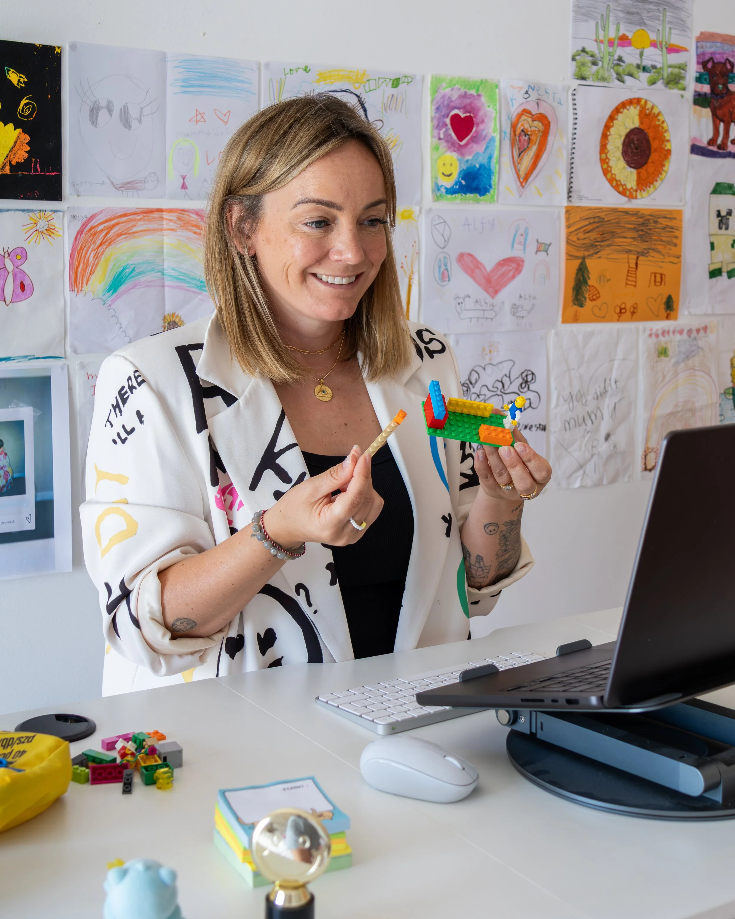 Victori Bradley smiling while holding a Lego creation, sitting at a desk with a keyboard, mouse, and various LEGO® pieces