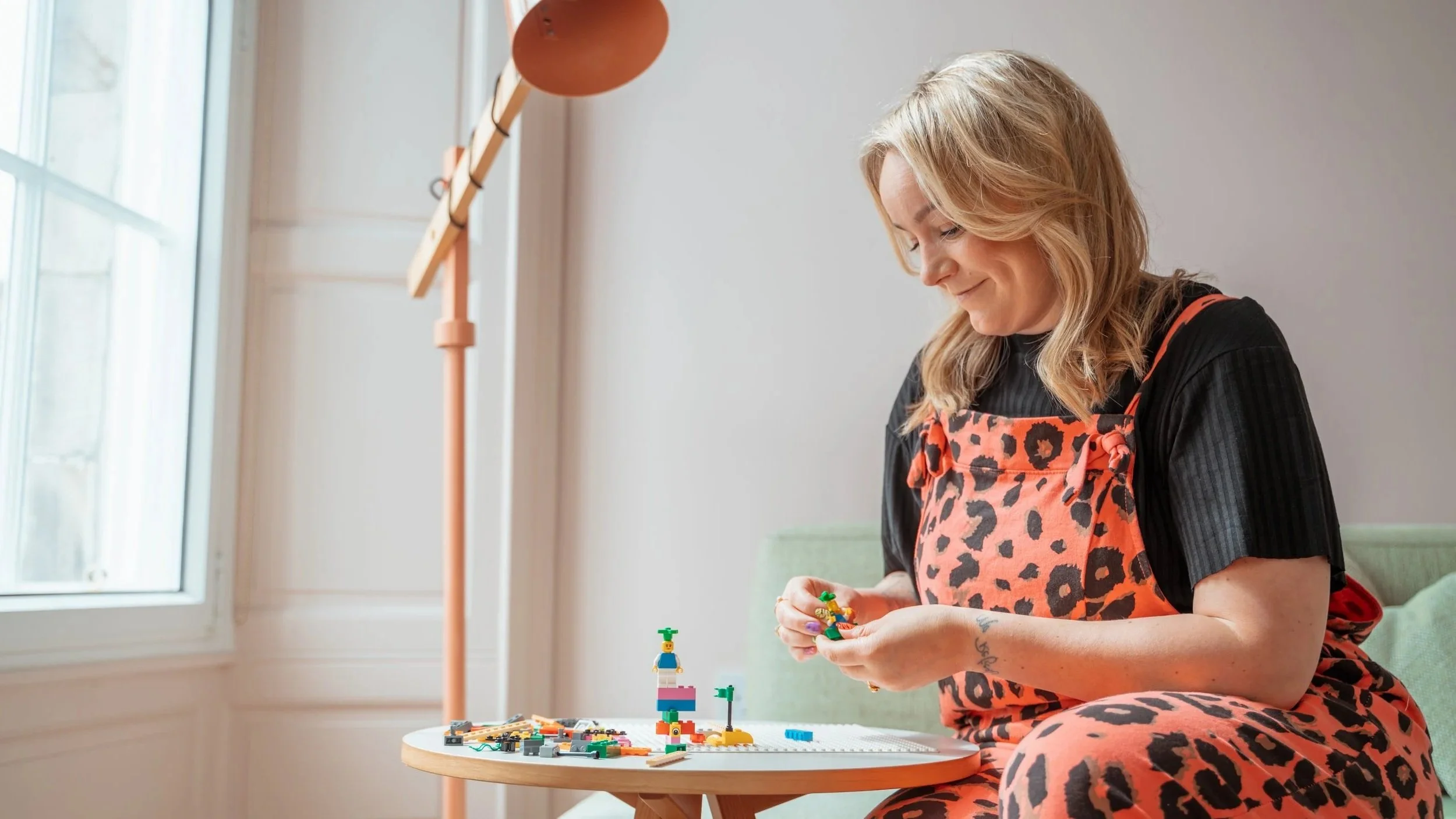 Woman in a leopard-print apron building colorful LEGO pieces at a table