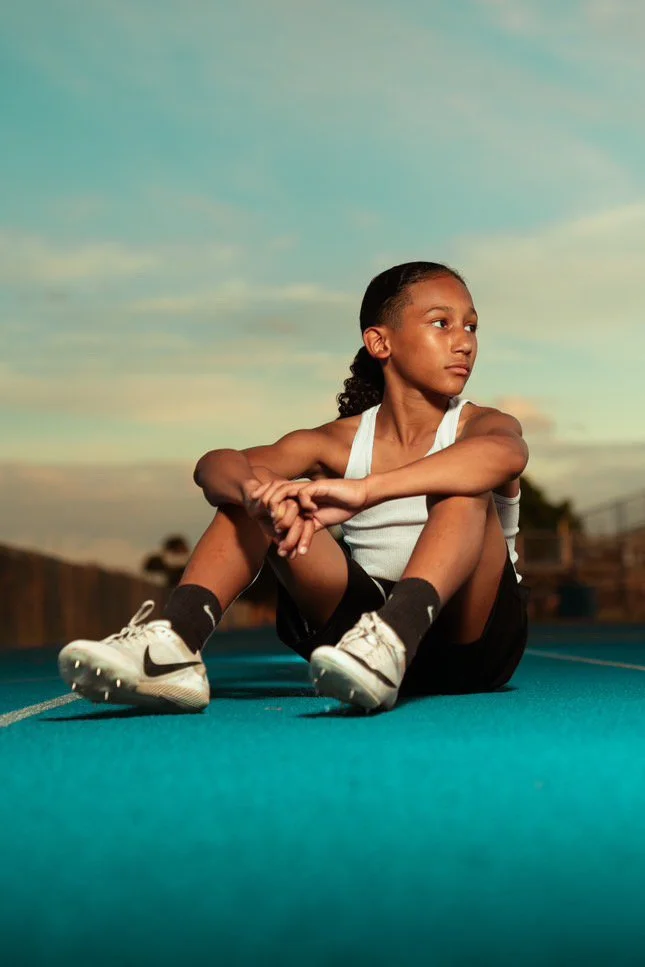 Young athlete stretching on a track during sunset, wearing athletic shoes and sportswear.