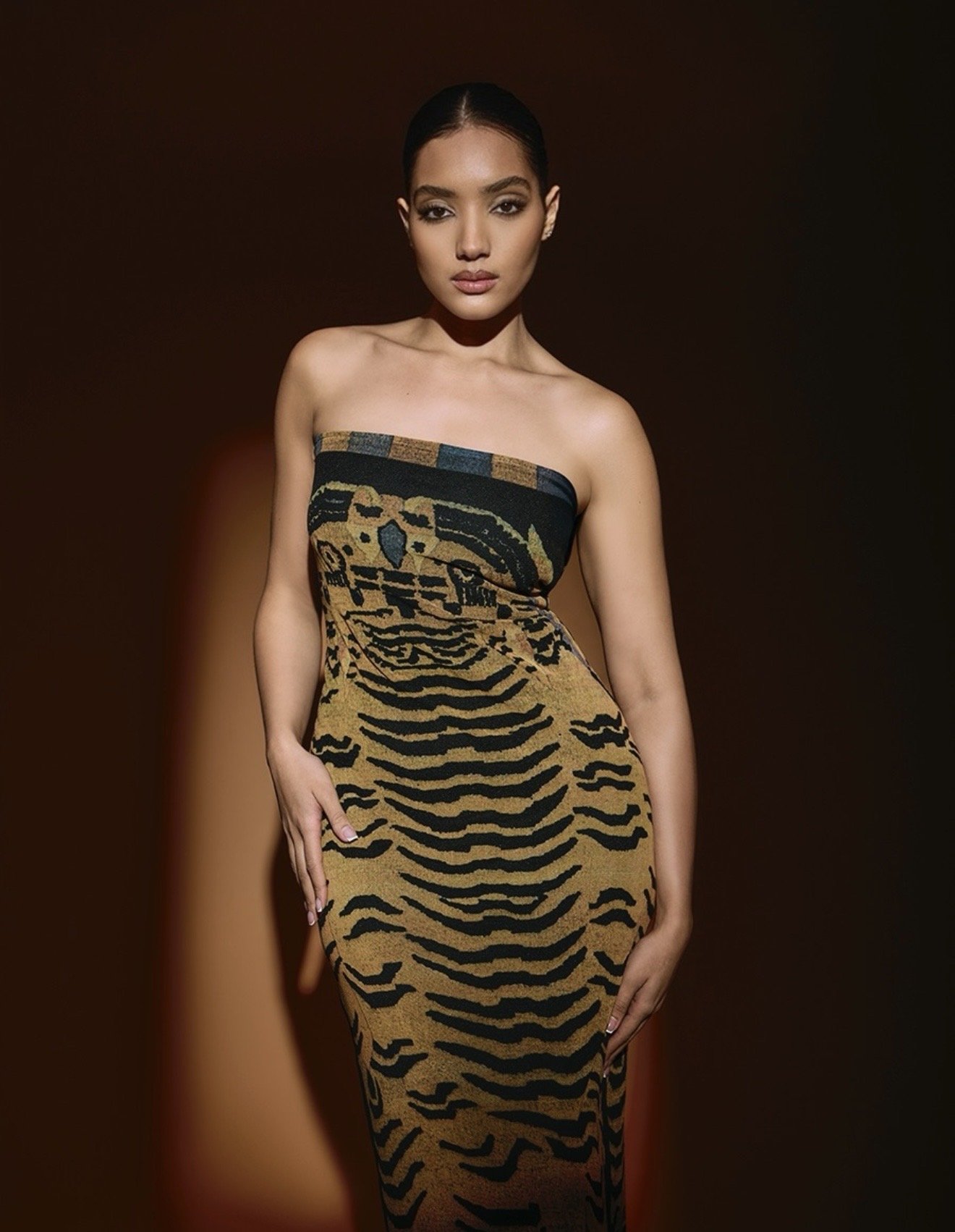 A woman wearing a strapless dress with a tiger stripe pattern, standing against a dark background.