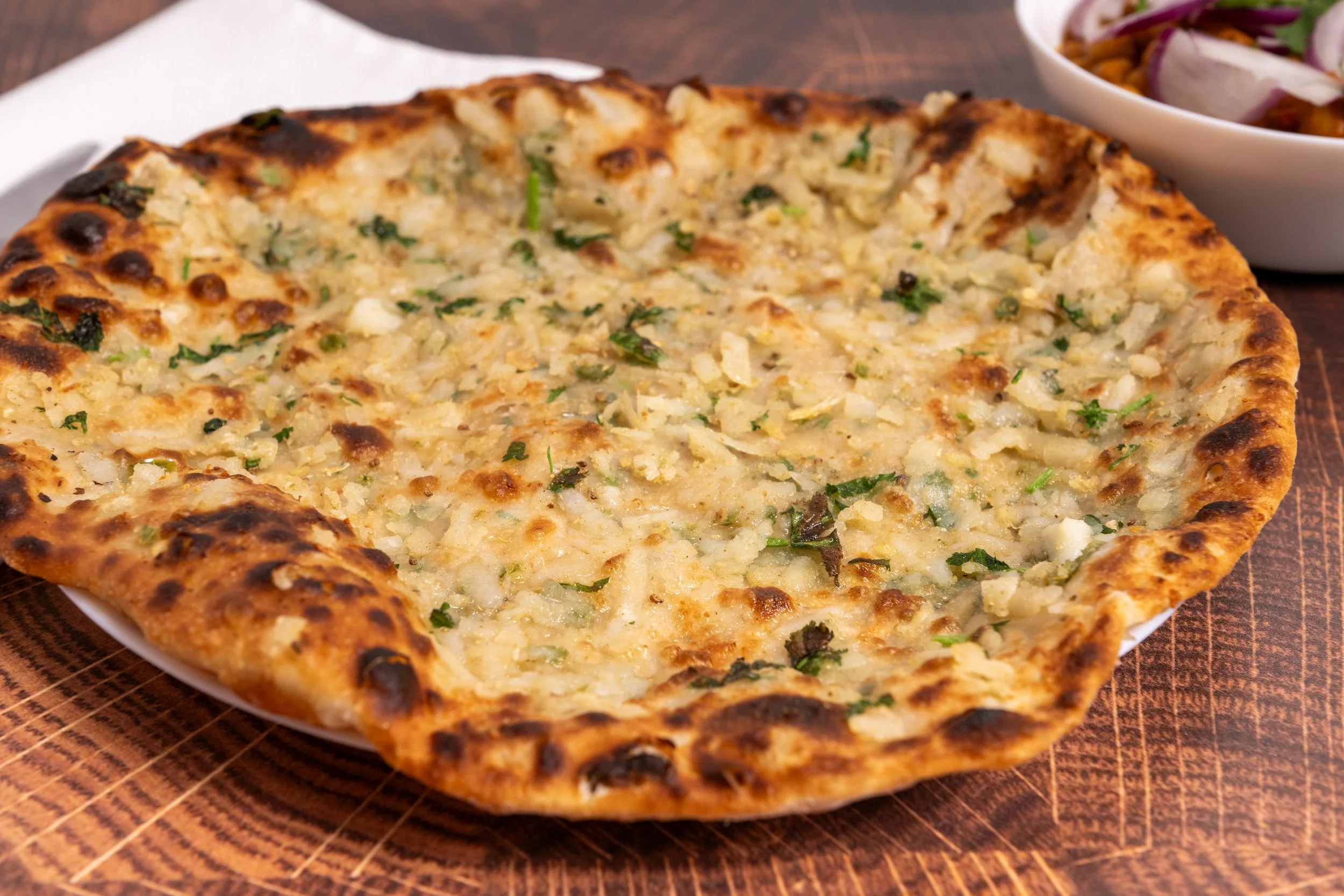 Cheese pizza with a golden-brown crust, served on a white plate, with a bowl of salad in the background.