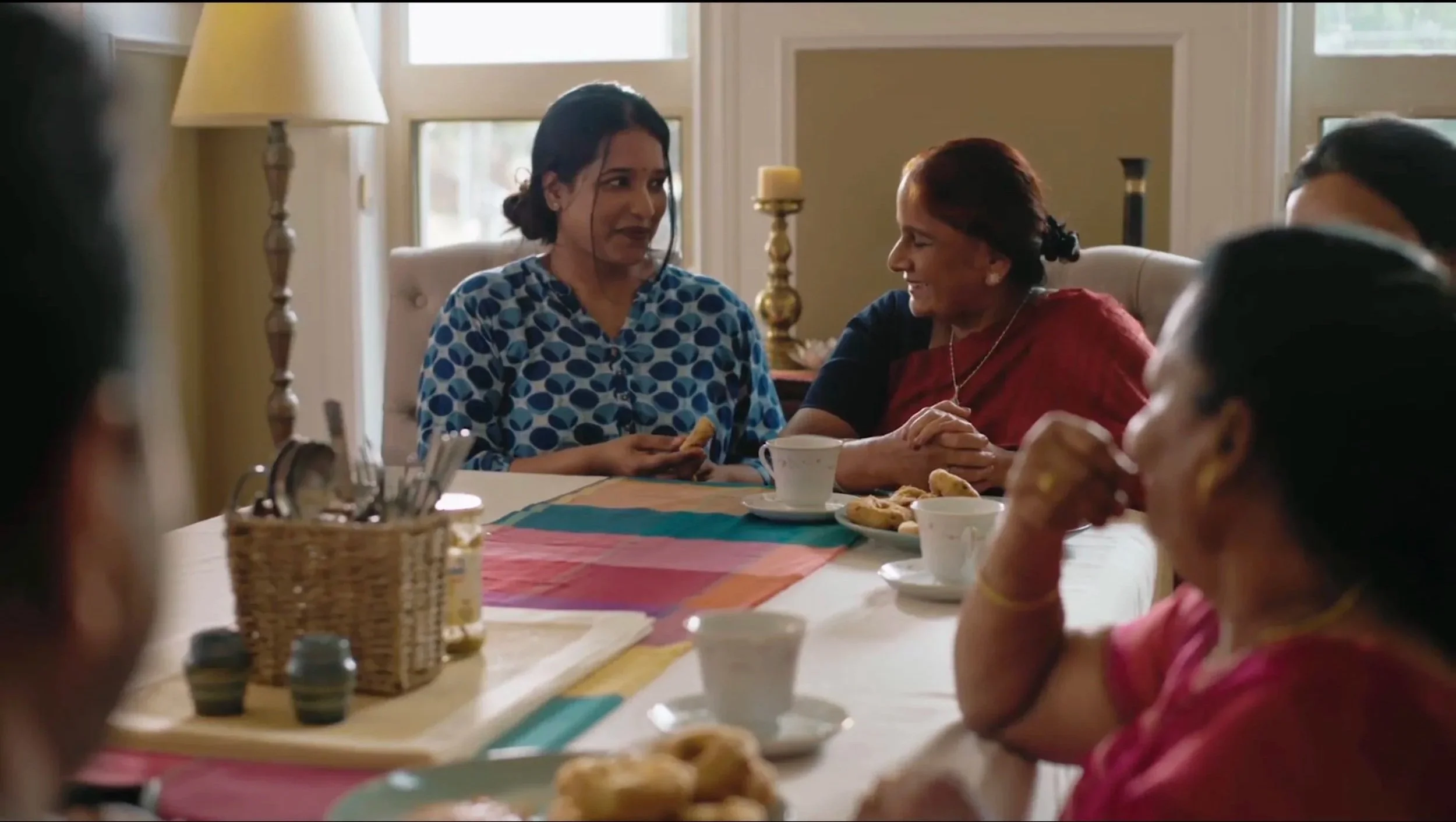 A group of women enjoying a meal together at a dining table in a cozy, well-lit room, with some women sharing a laugh.