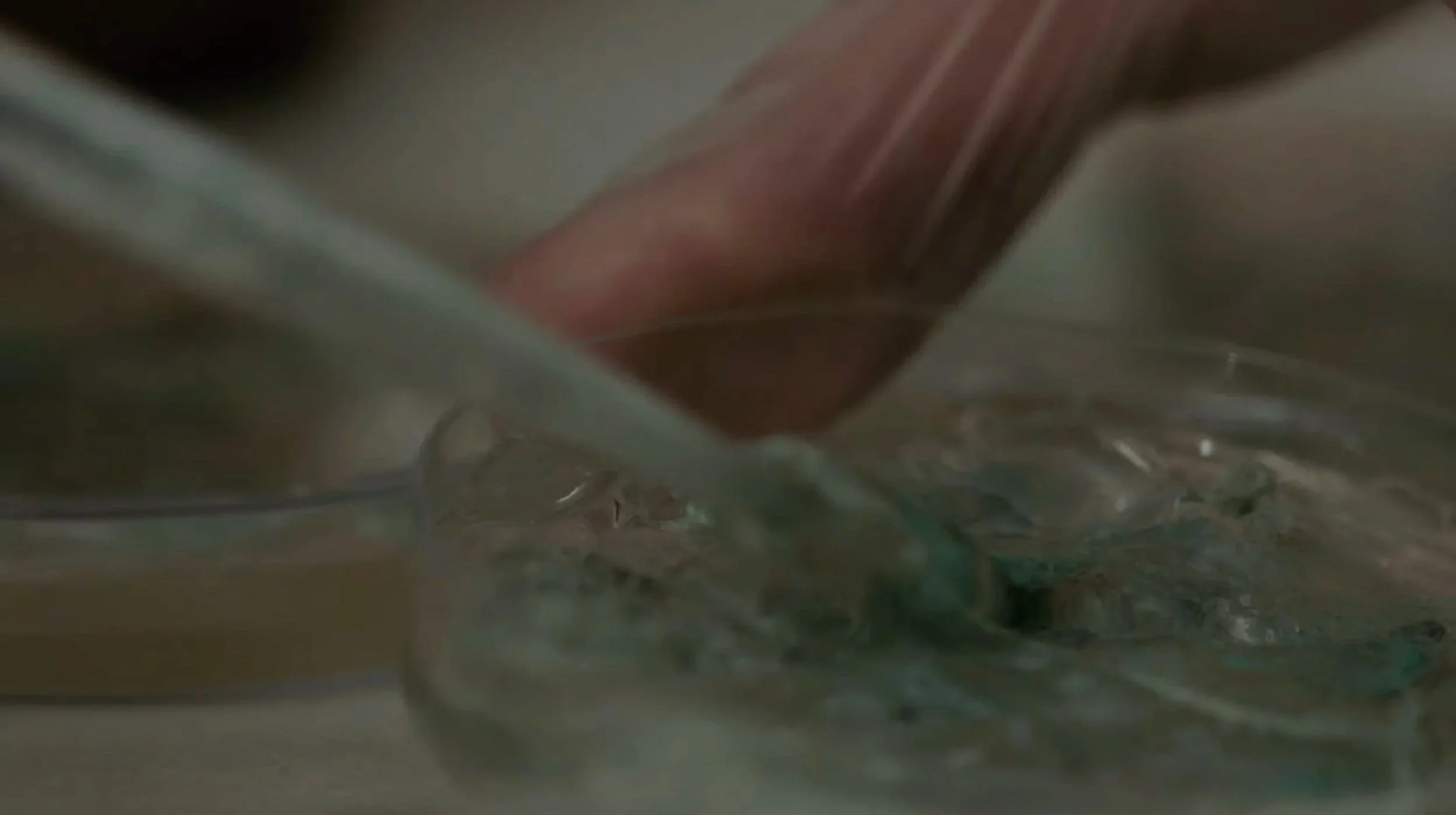 A blurry image of what appears to be a close-up of a person's hand or arm amidst a textured or rough surface, possibly fabric or material, with muted colors and indistinct features.