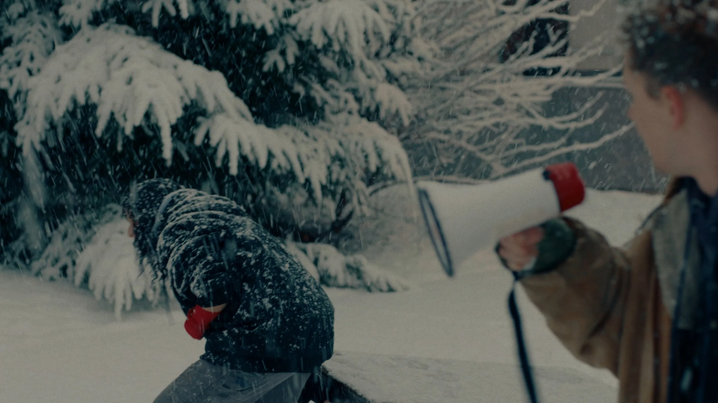 People in outdoor winter clothing using ice axes, surrounded by snow-covered trees during snowfall.