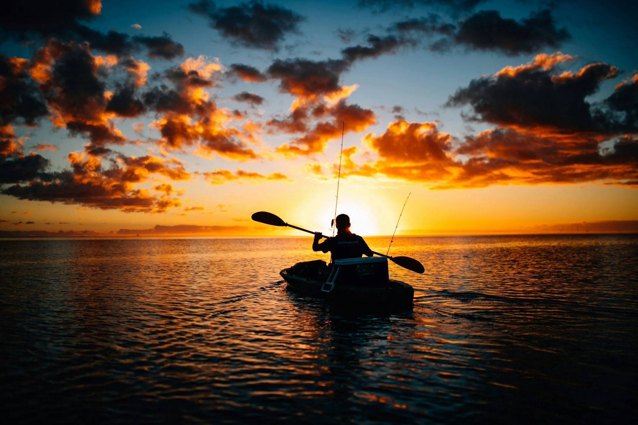 A person kayaking on a body of water during sunset with vibrant orange and dark clouds in the sky.